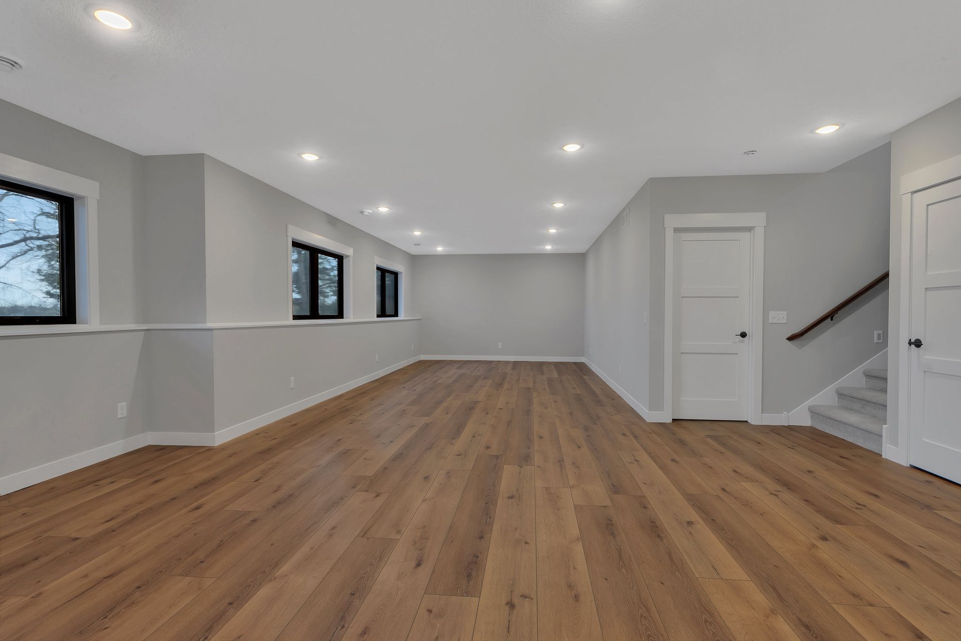An empty basement with hardwood floors and stairs.