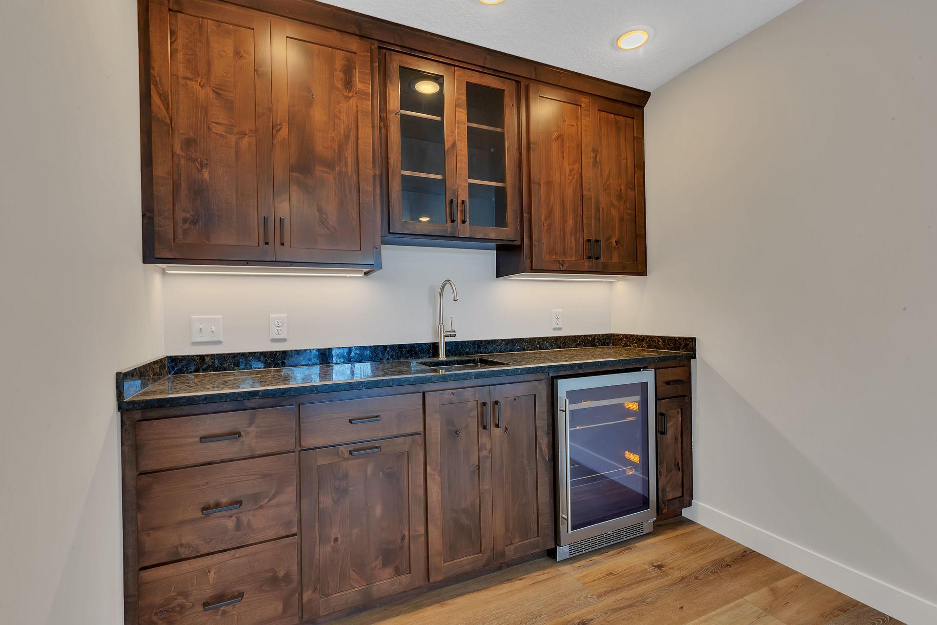 A kitchen with wooden cabinets , granite counter tops , a sink and a refrigerator.