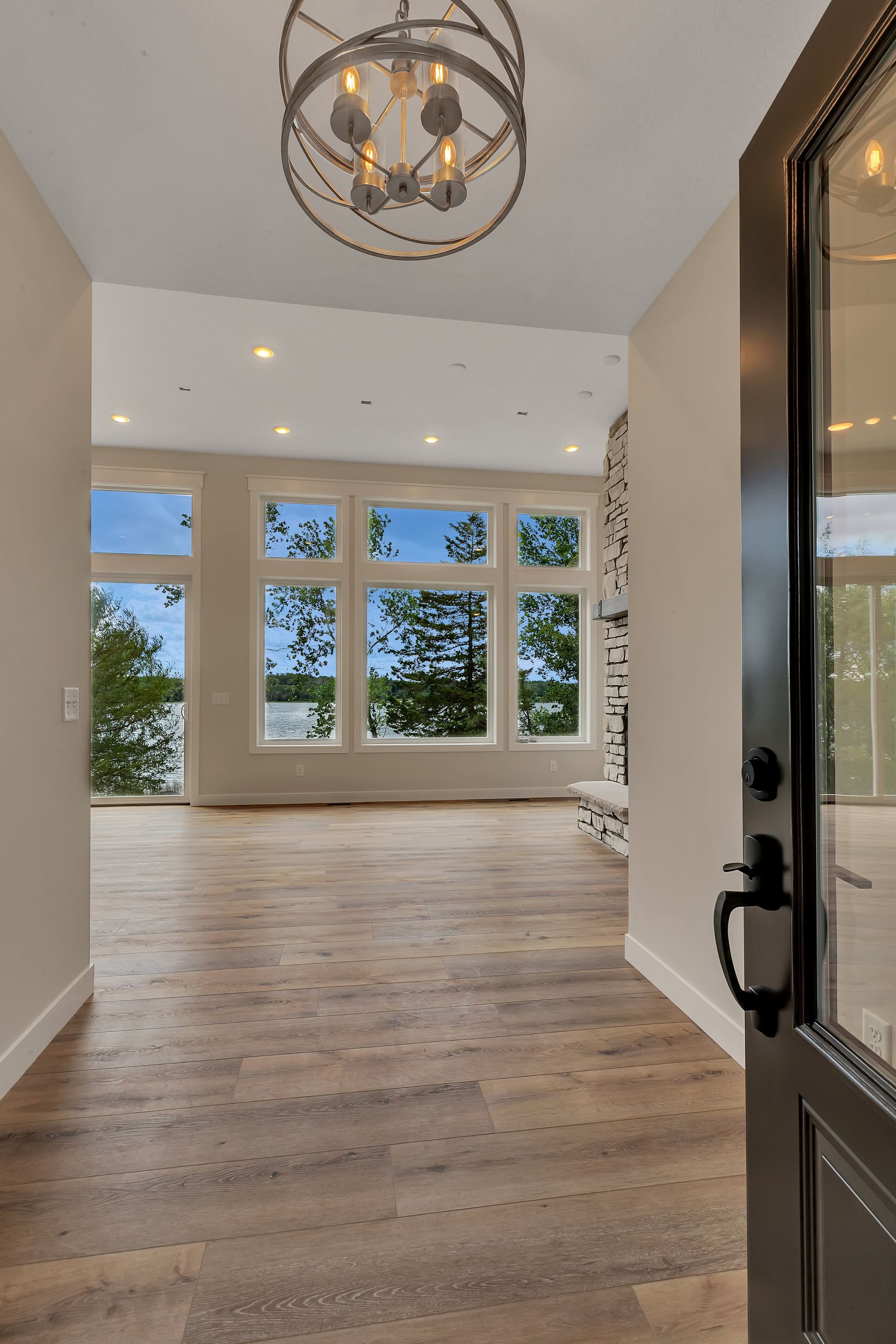 An empty hallway with hardwood floors and a chandelier hanging from the ceiling.