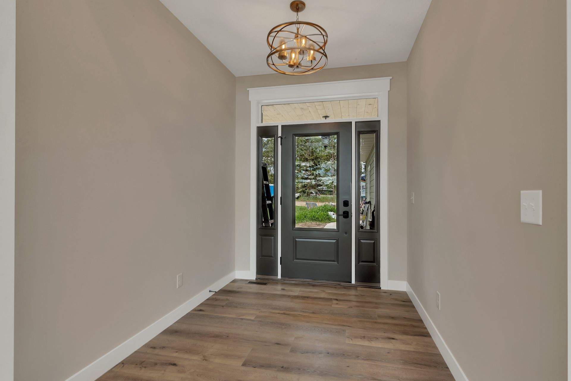 A hallway with a black door and a chandelier hanging from the ceiling.