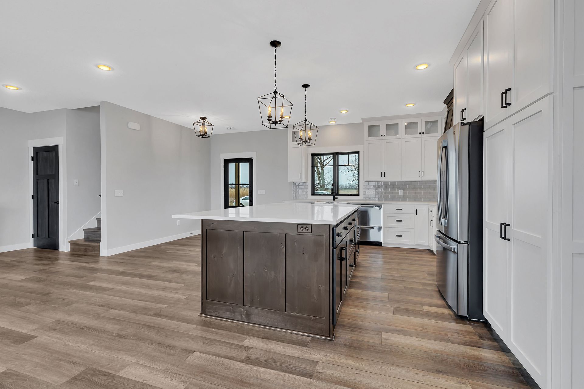A kitchen with a large island , white cabinets , stainless steel appliances and hardwood floors.