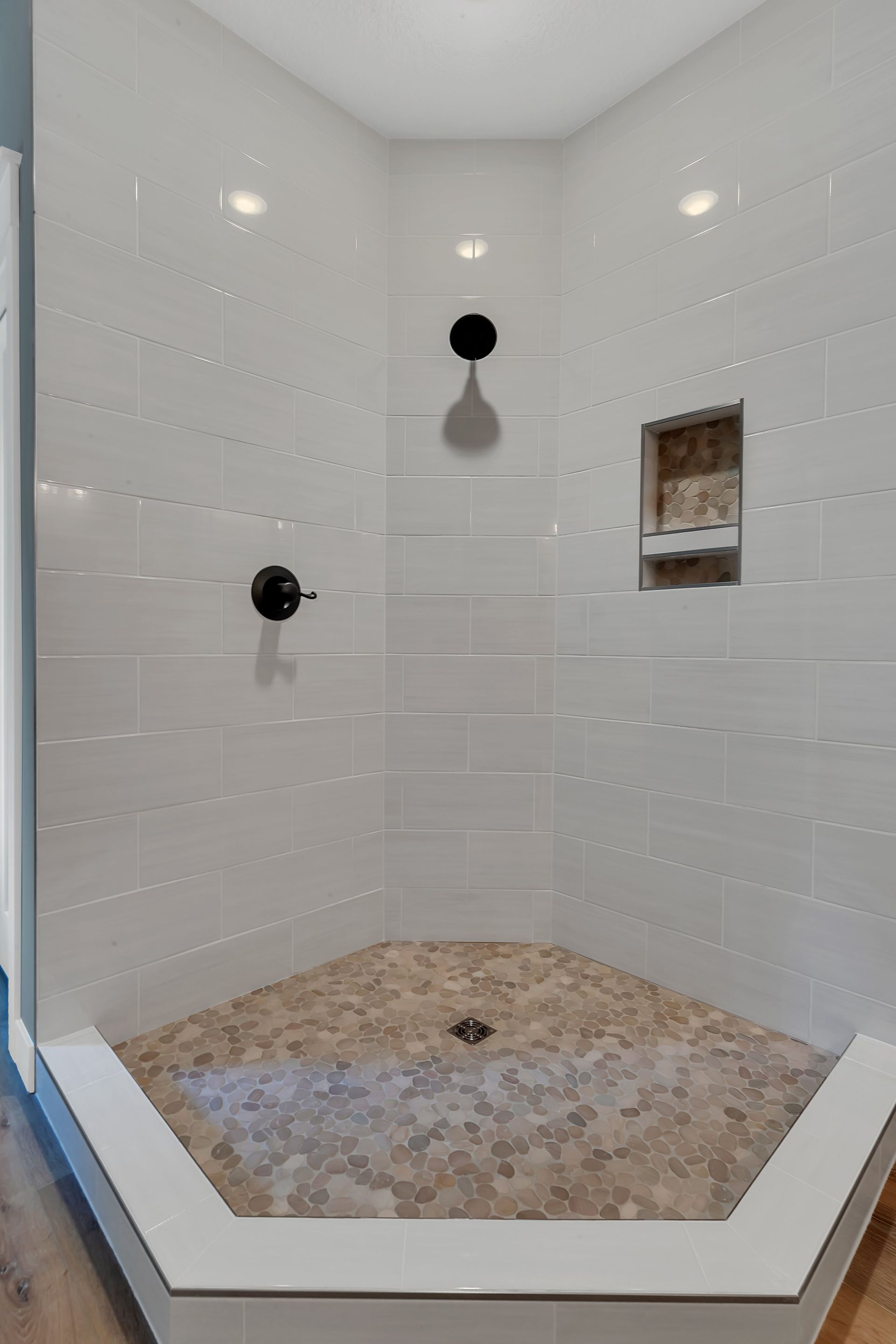 A shower stall with white tiles and a mosaic floor.