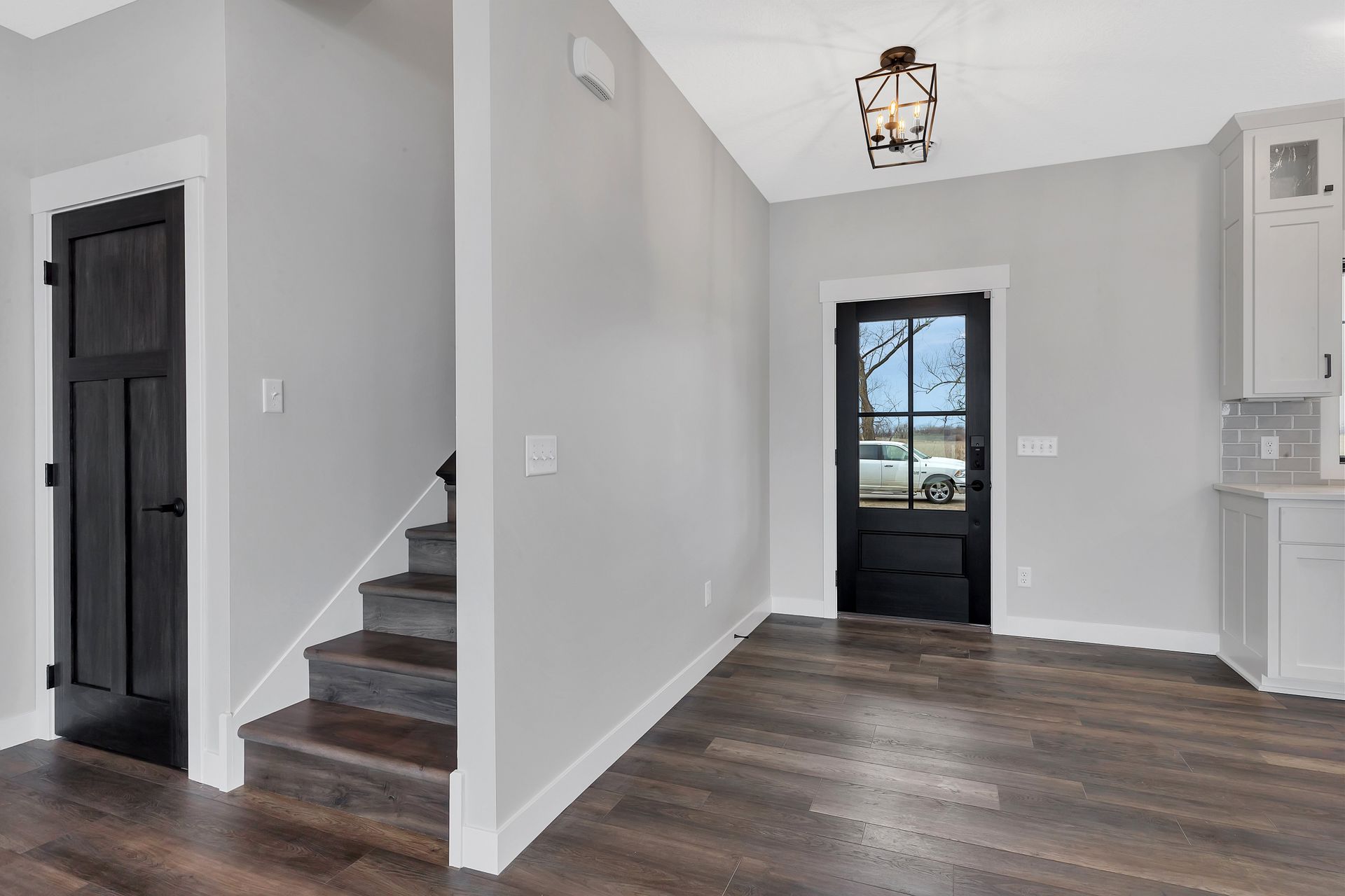 A hallway with stairs and a black door in a house.