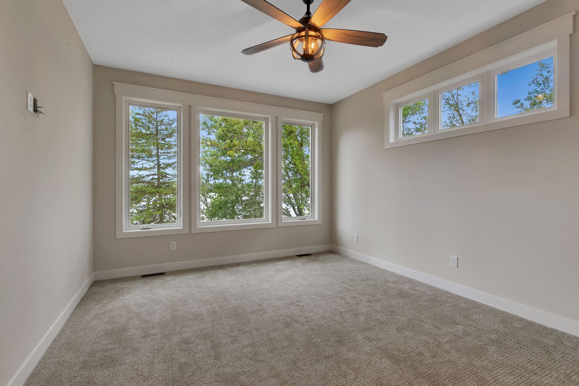 An empty room with a ceiling fan and three windows.