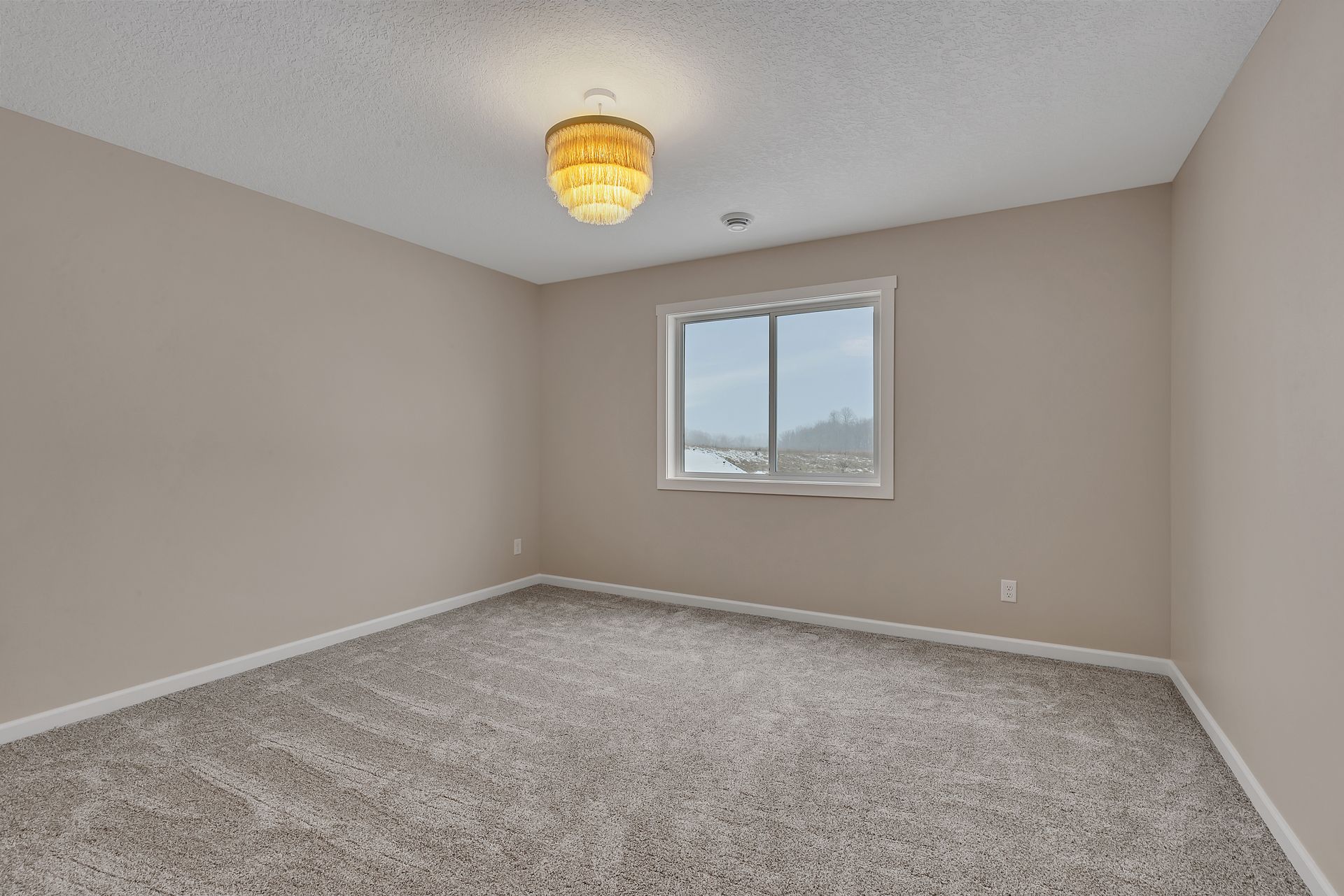 An empty bedroom with a window and a chandelier.