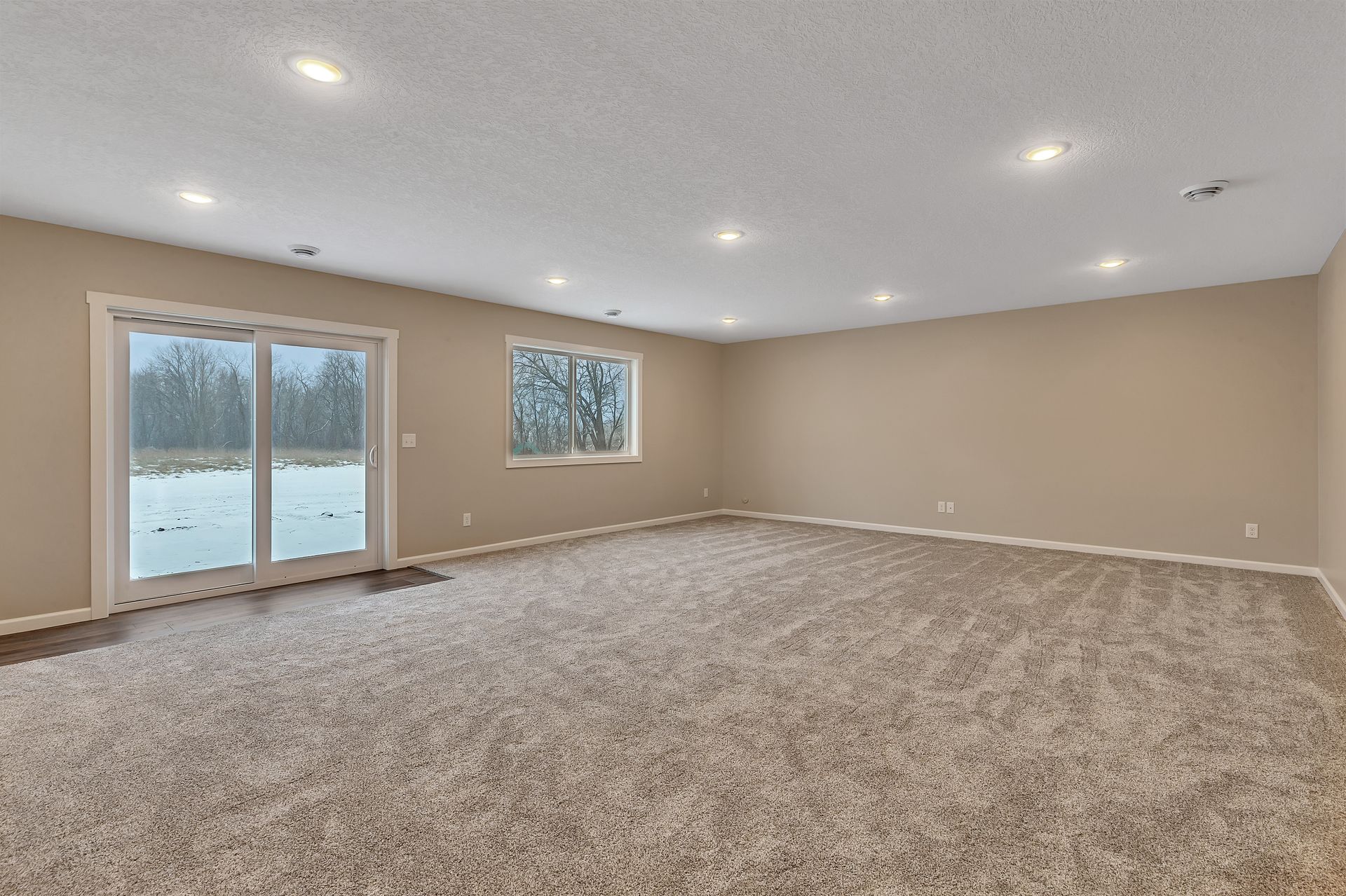 An empty basement with carpeted floors and sliding glass doors.
