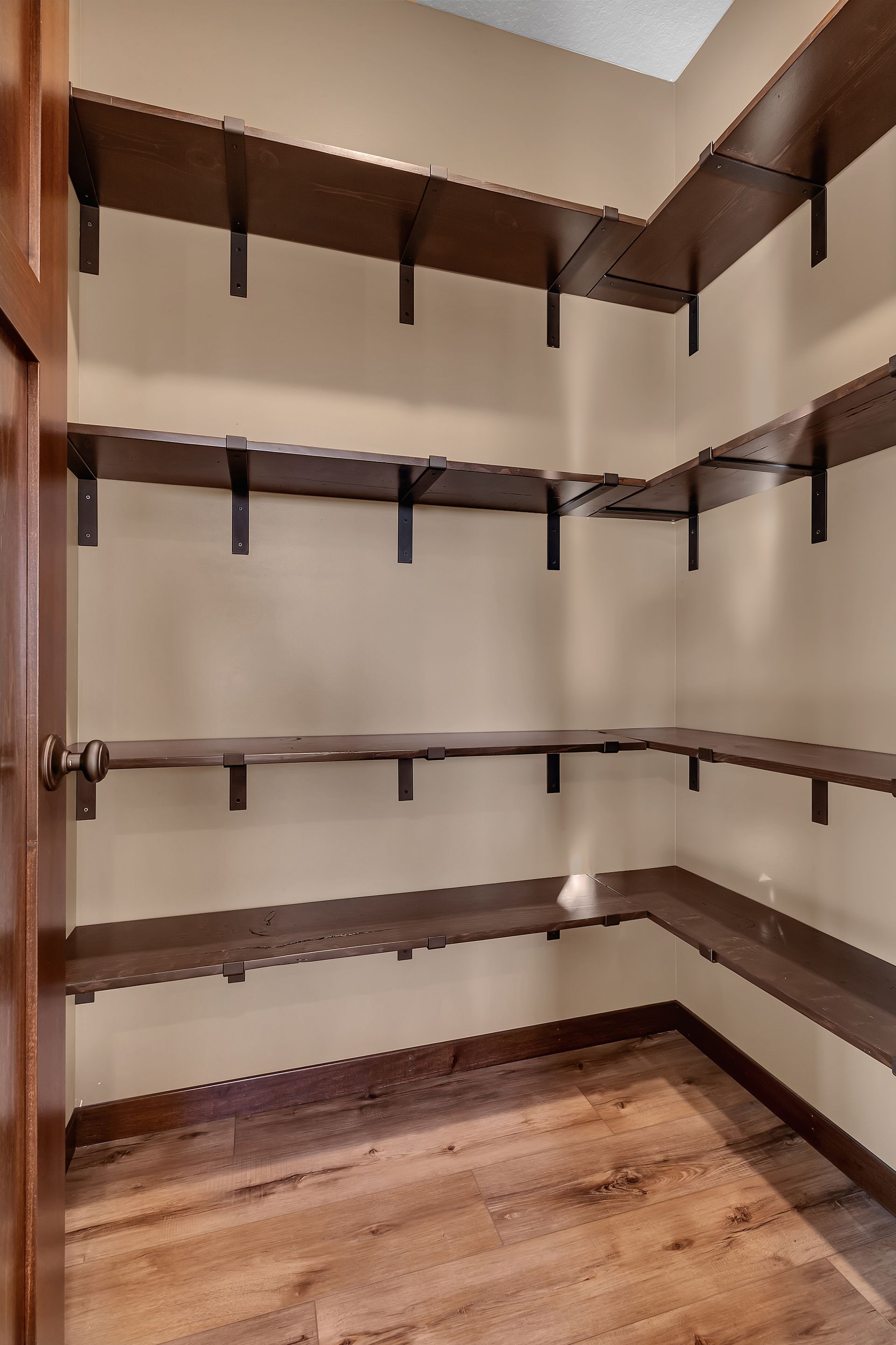 An empty walk in closet with wooden shelves and hardwood floors.