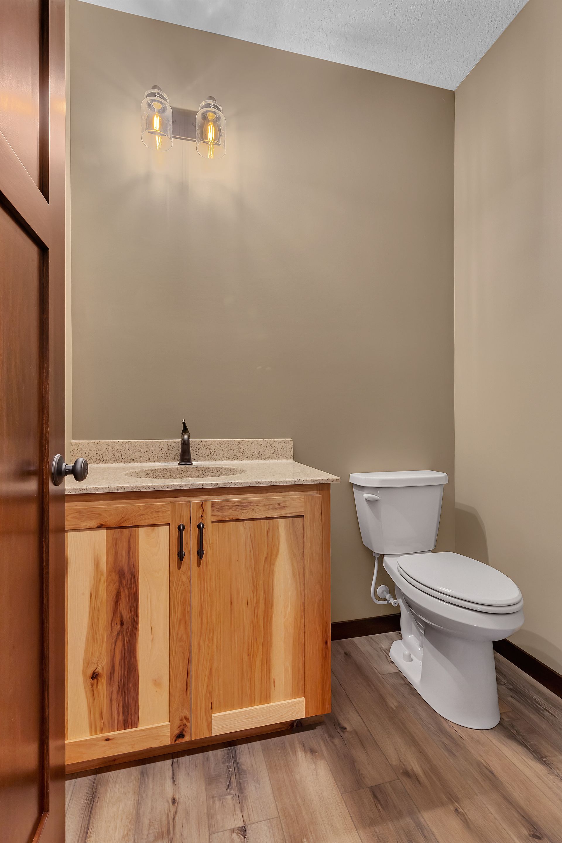 A bathroom with a toilet , sink and wooden cabinets.