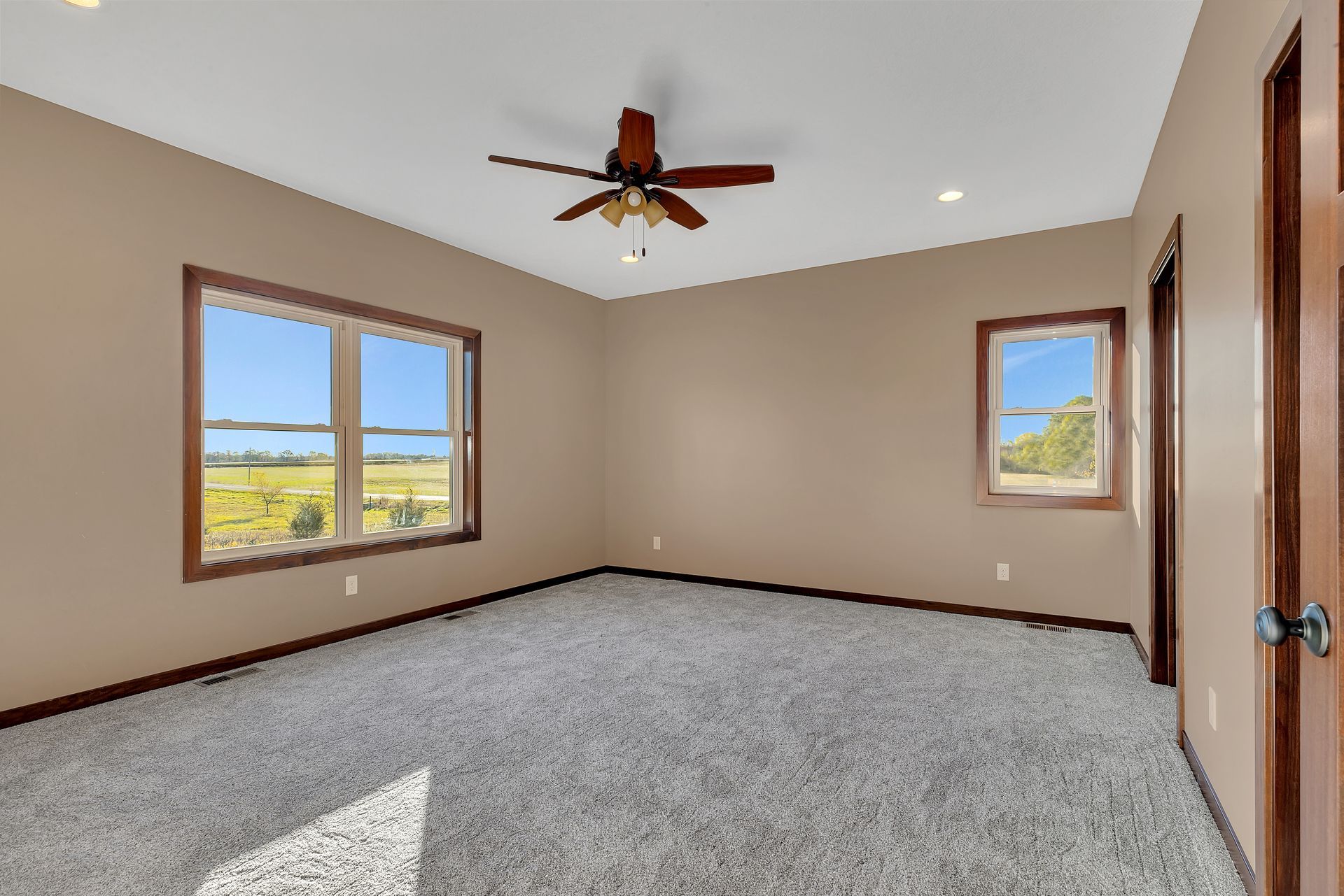 An empty bedroom with a ceiling fan and two windows.