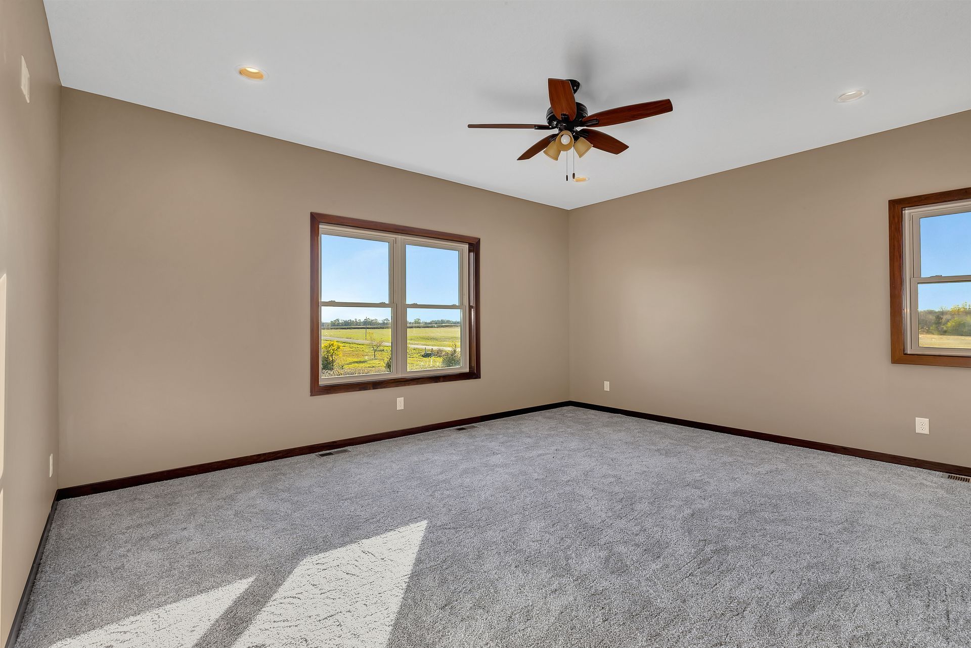 An empty bedroom with a ceiling fan and two windows.
