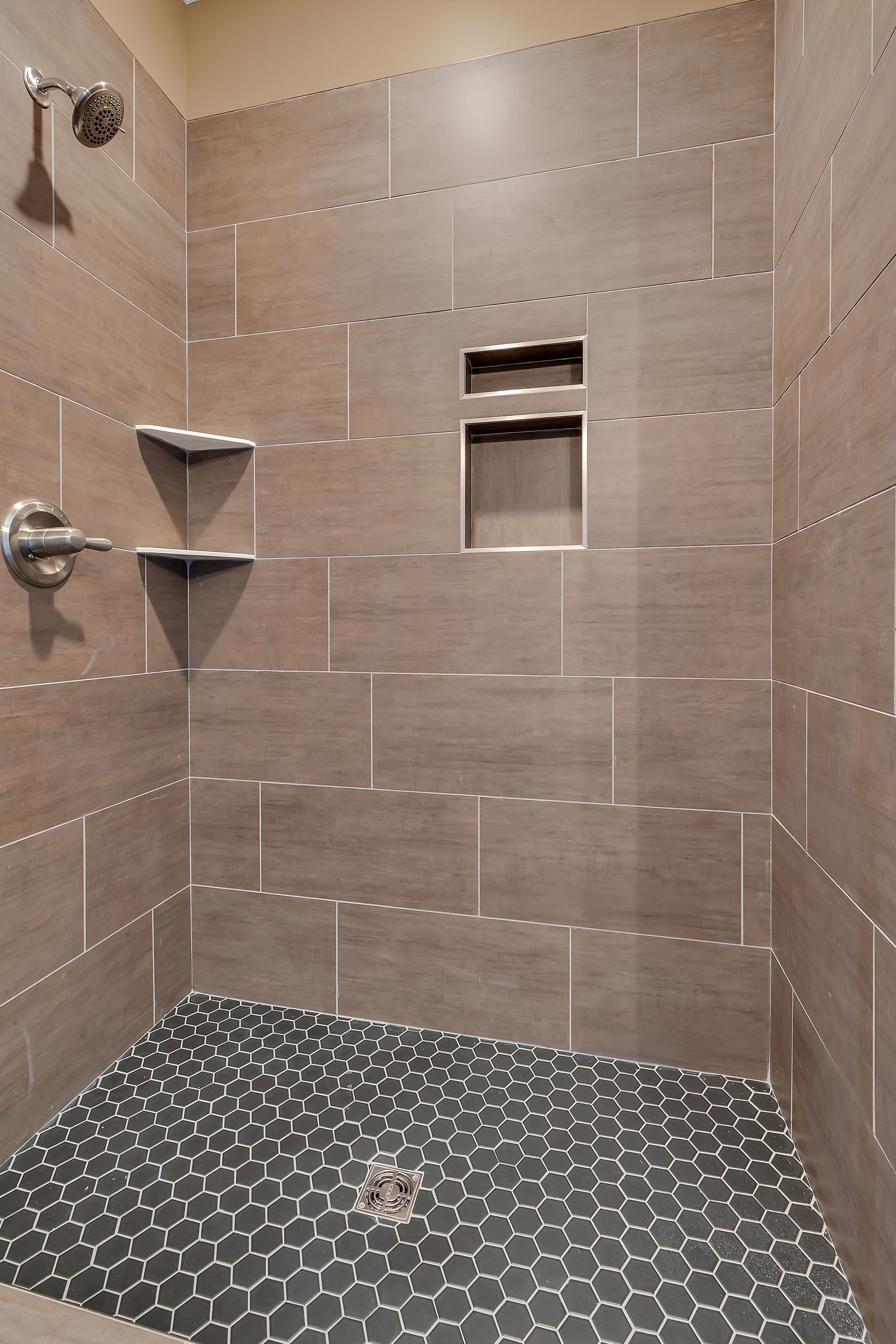 A shower with brown tiles and a black tile floor