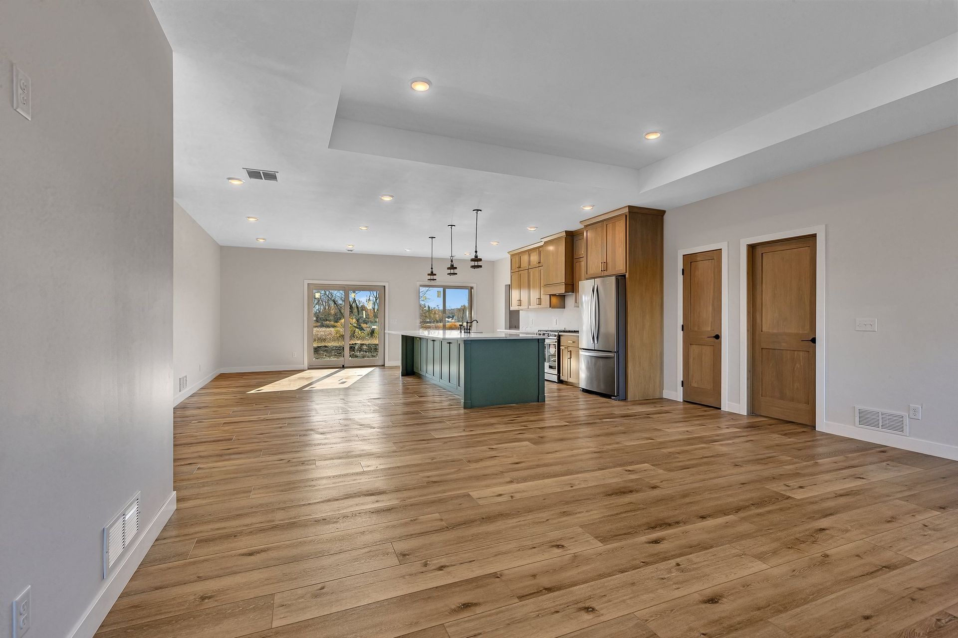 A large empty room with hardwood floors and a kitchen in the background.