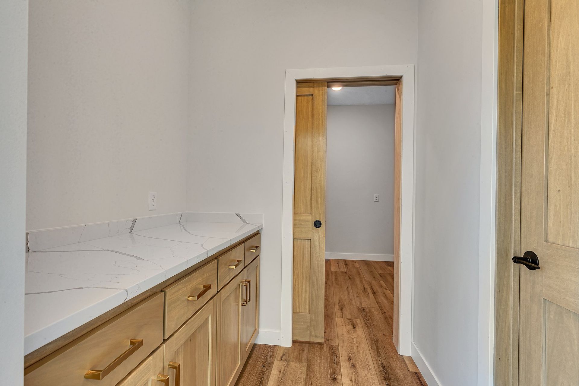 A hallway in a house with wooden floors and cabinets leading to a room.