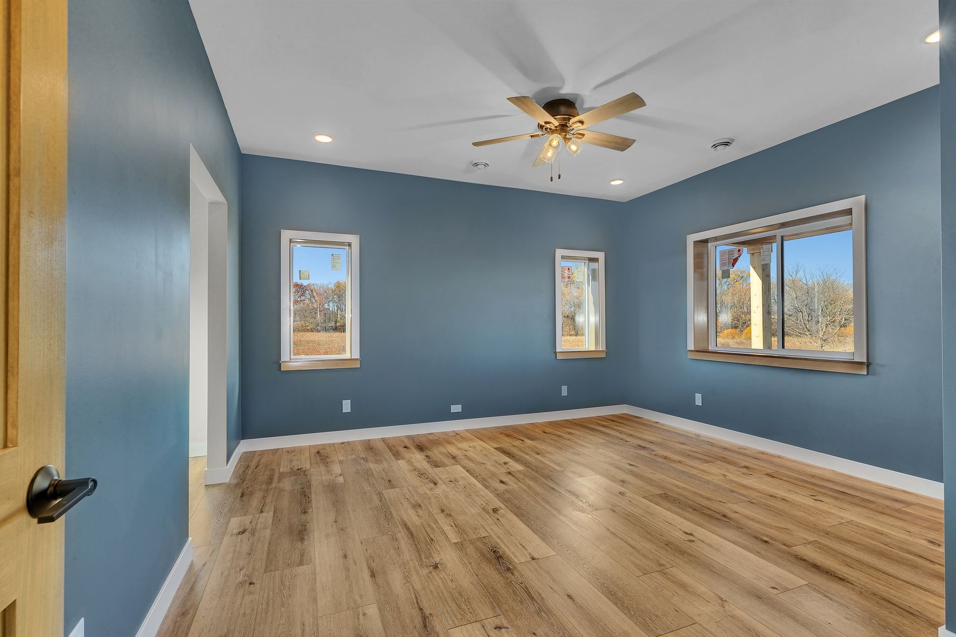 An empty room with blue walls and hardwood floors and a ceiling fan.