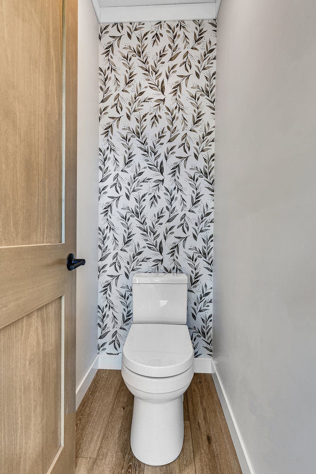 A toilet in a bathroom with a floral wallpaper on the wall.