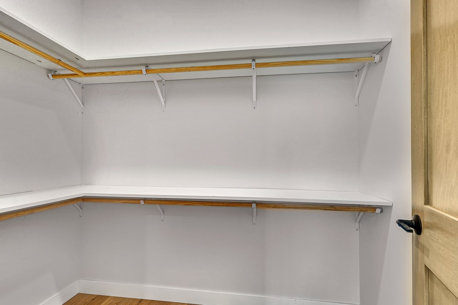 An empty walk in closet with a wooden floor and shelves.