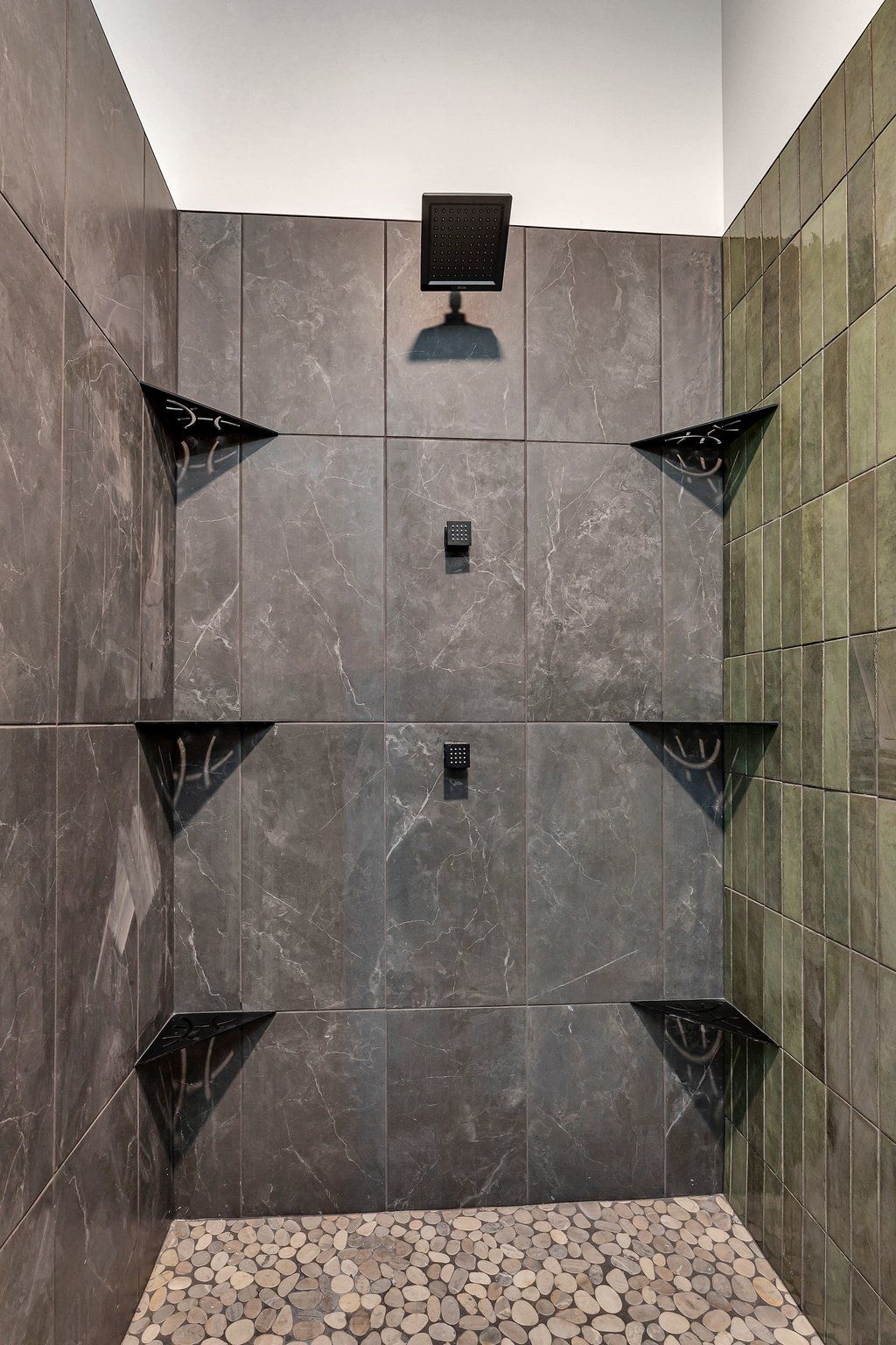 A bathroom with a walk in shower with a tiled wall and shelves.