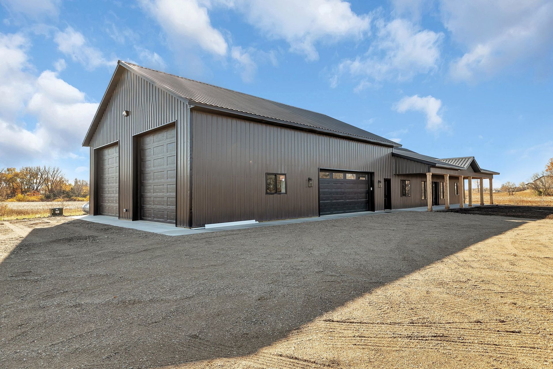A large barn with two garage doors is sitting on top of a dirt field.