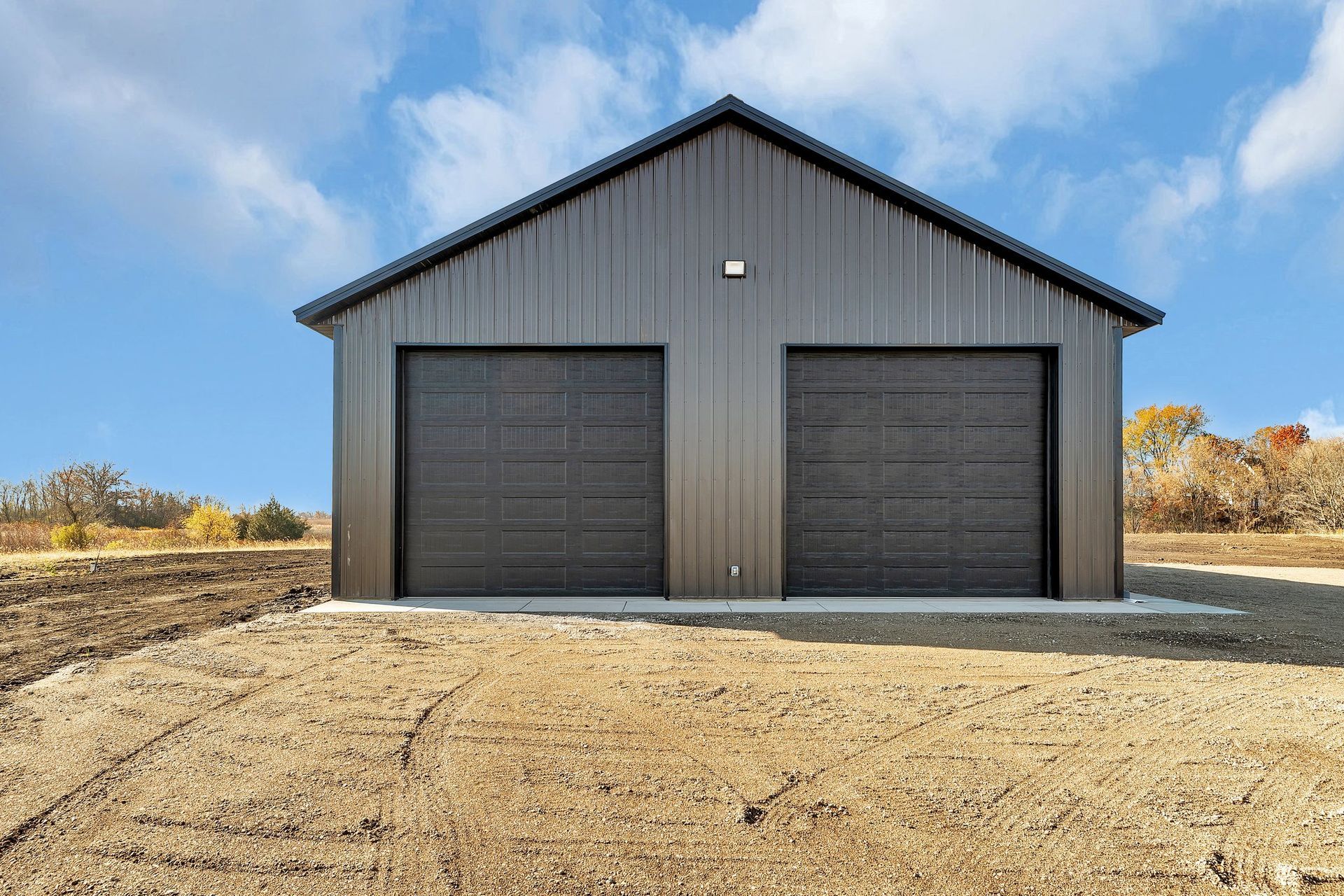 A large metal garage with two garage doors is sitting in the middle of a dirt field.