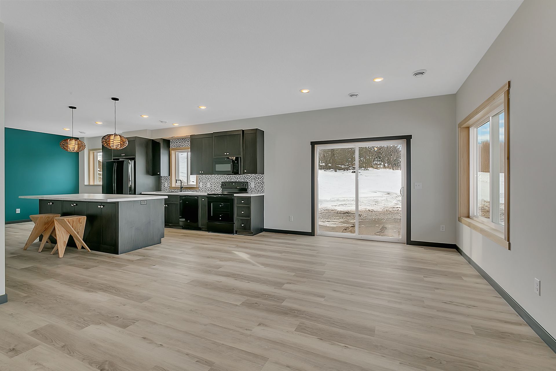 A large empty room with a kitchen and sliding glass doors.