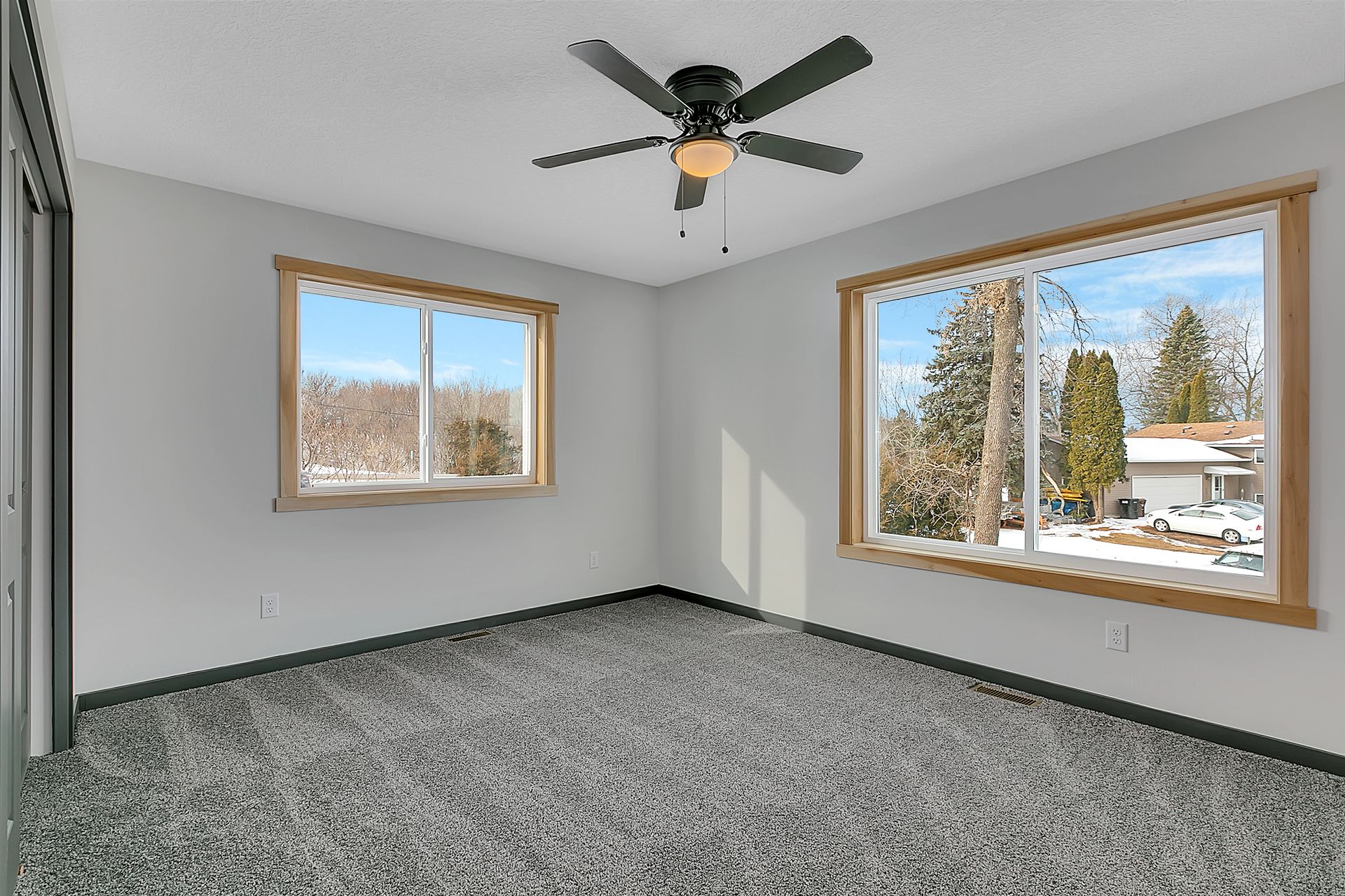 An empty room with two windows and a ceiling fan.