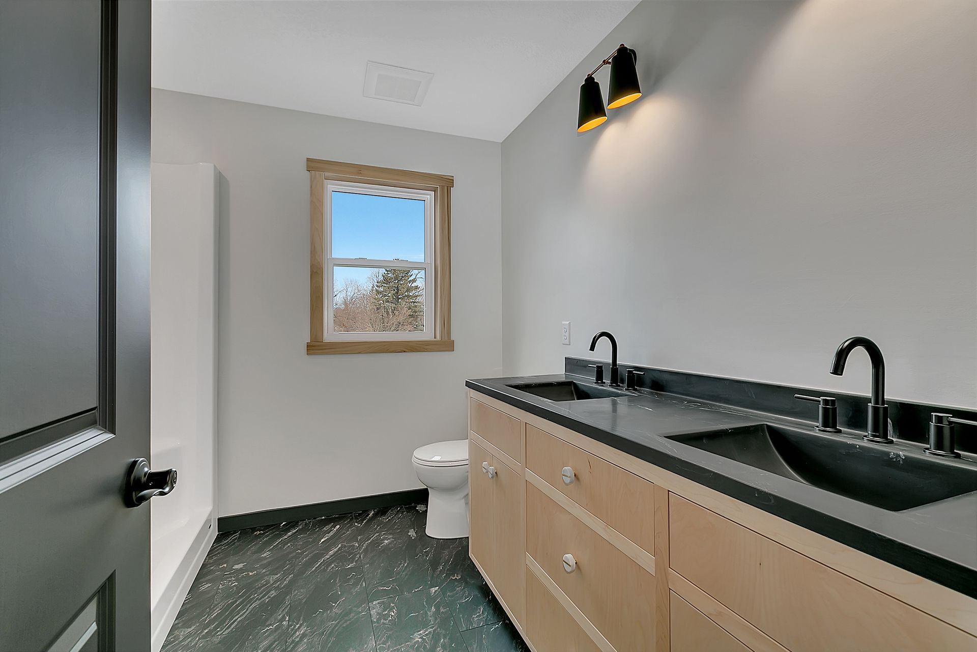 A bathroom with two sinks , a toilet and a window.