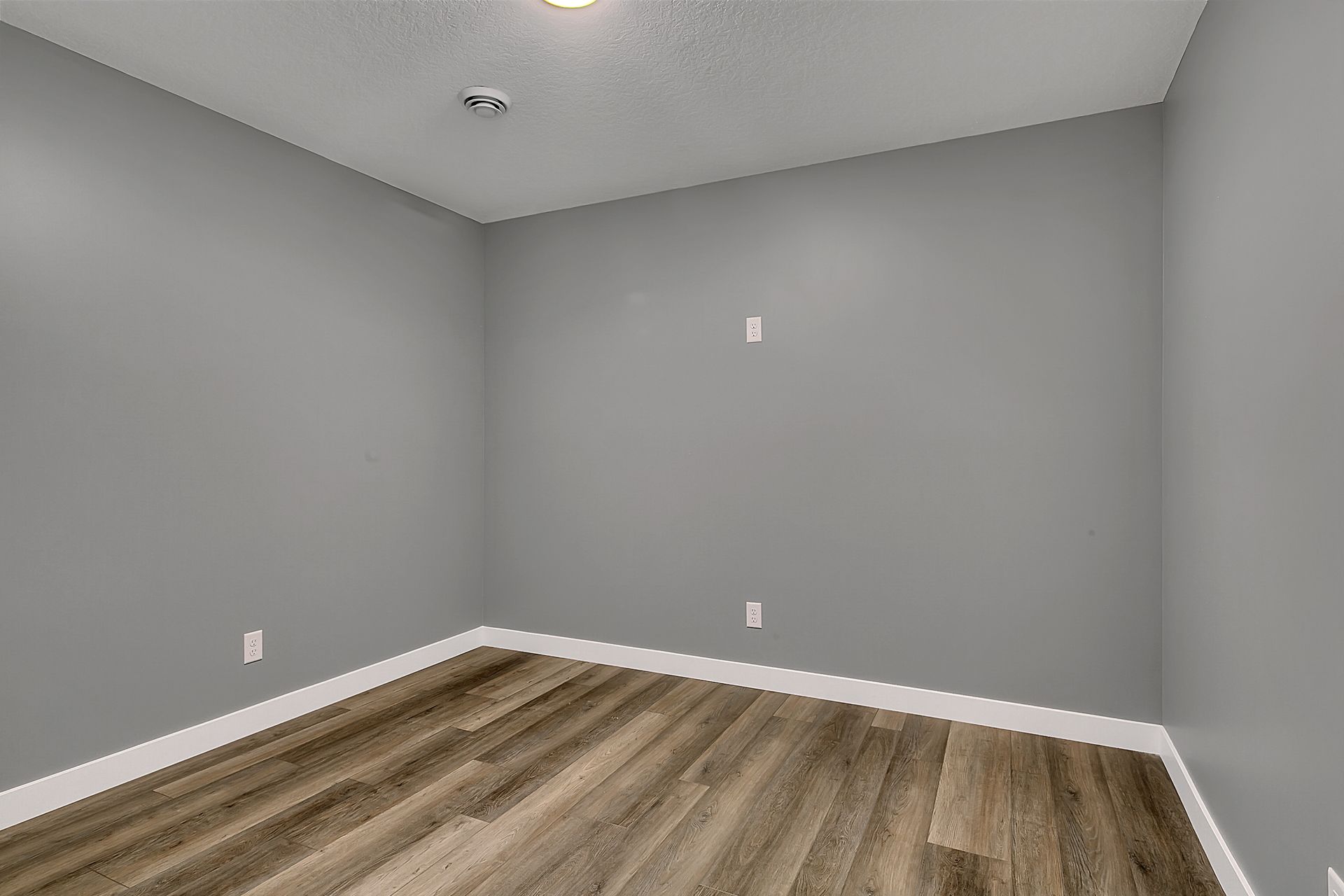 An empty room with gray walls and wooden floors.