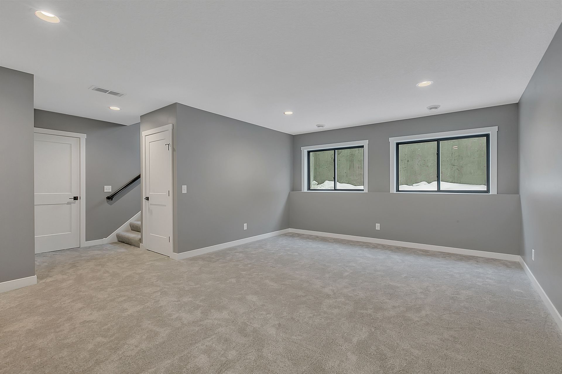 An empty basement with carpeted floors and gray walls.
