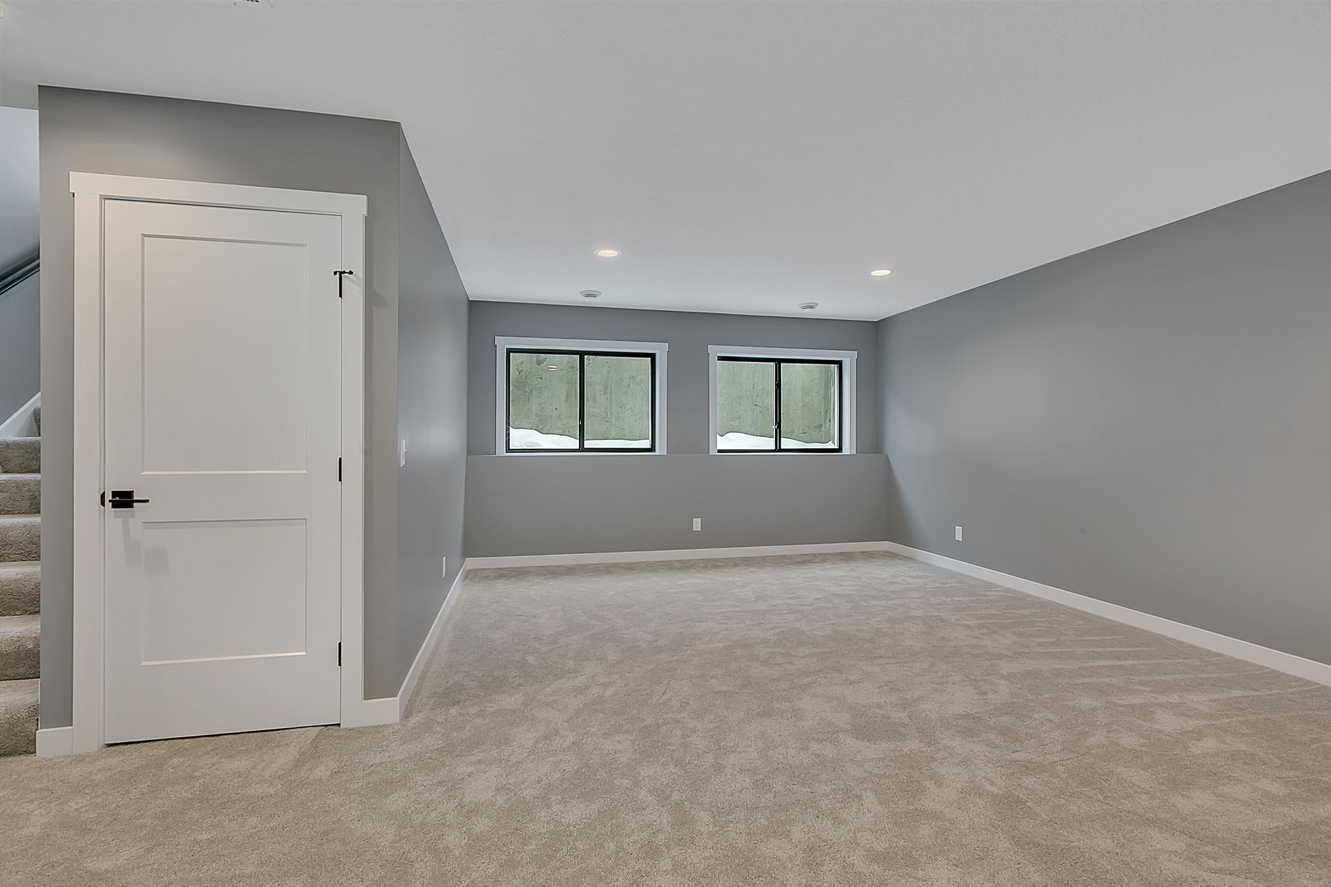 An empty basement with carpeted floors and gray walls.