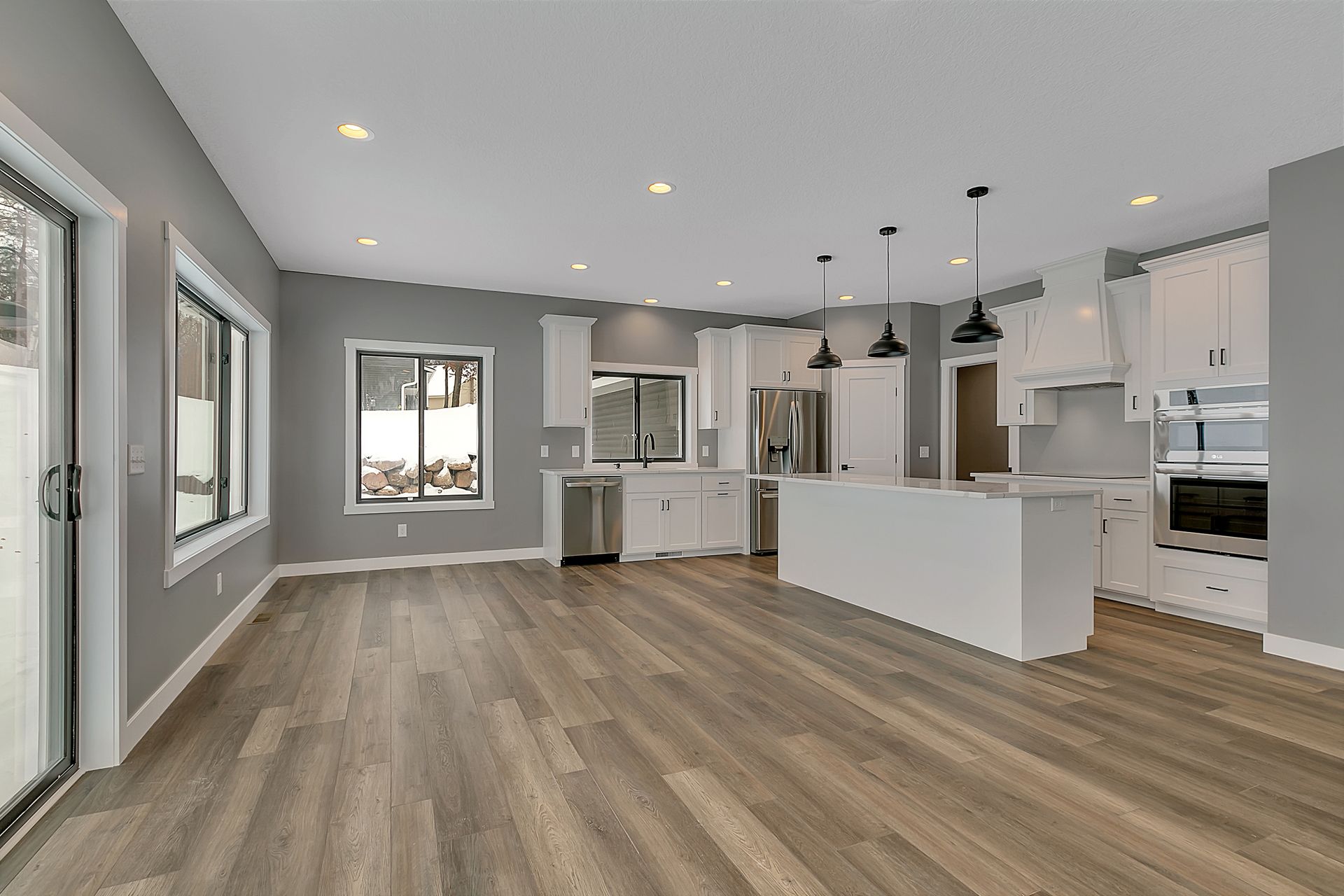 An empty kitchen with hardwood floors and white cabinets.