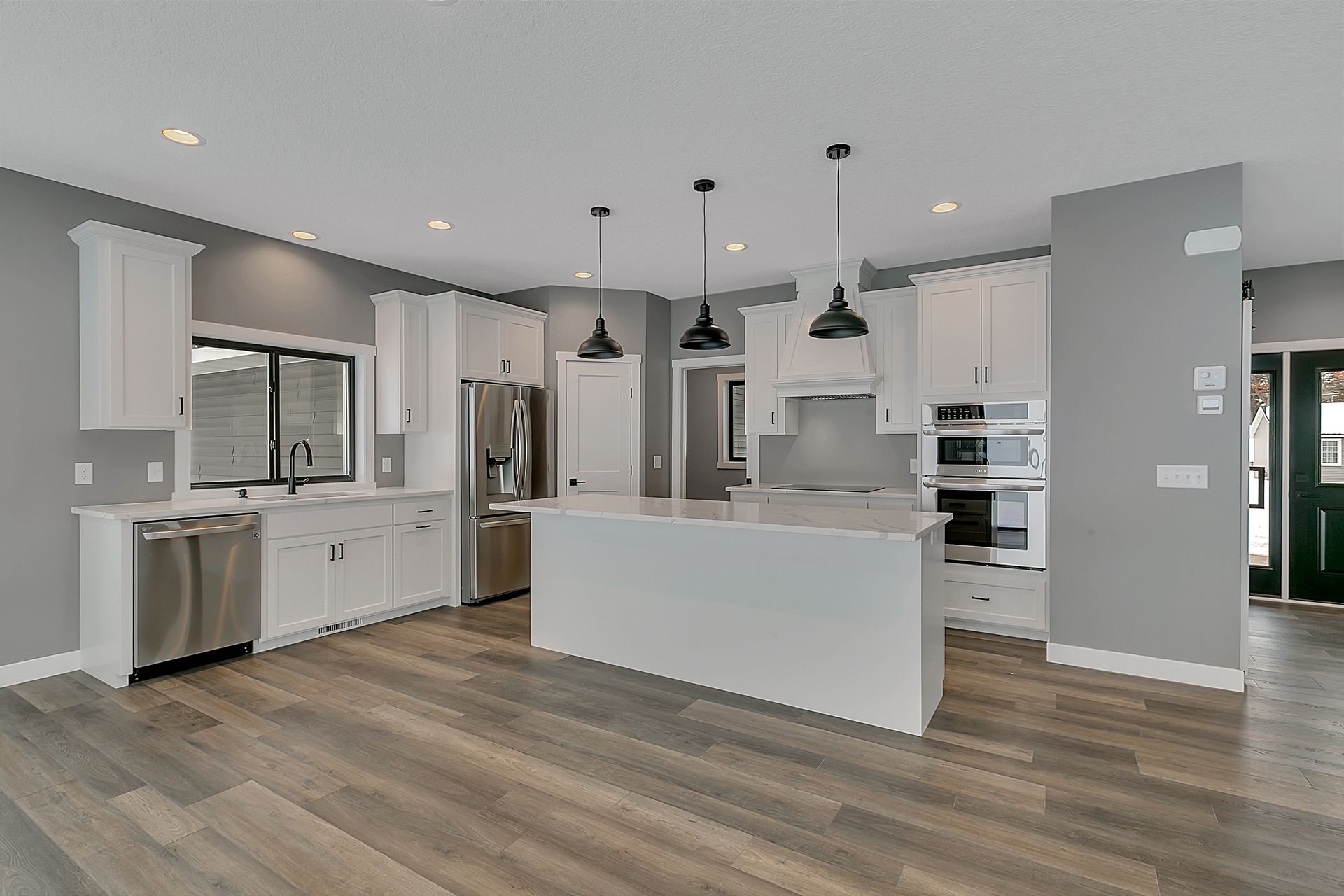 A kitchen with white cabinets , stainless steel appliances , hardwood floors and a large island.