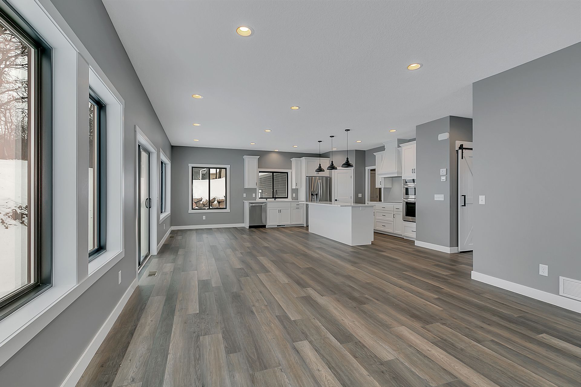 A large empty room with hardwood floors and a kitchen in the background.