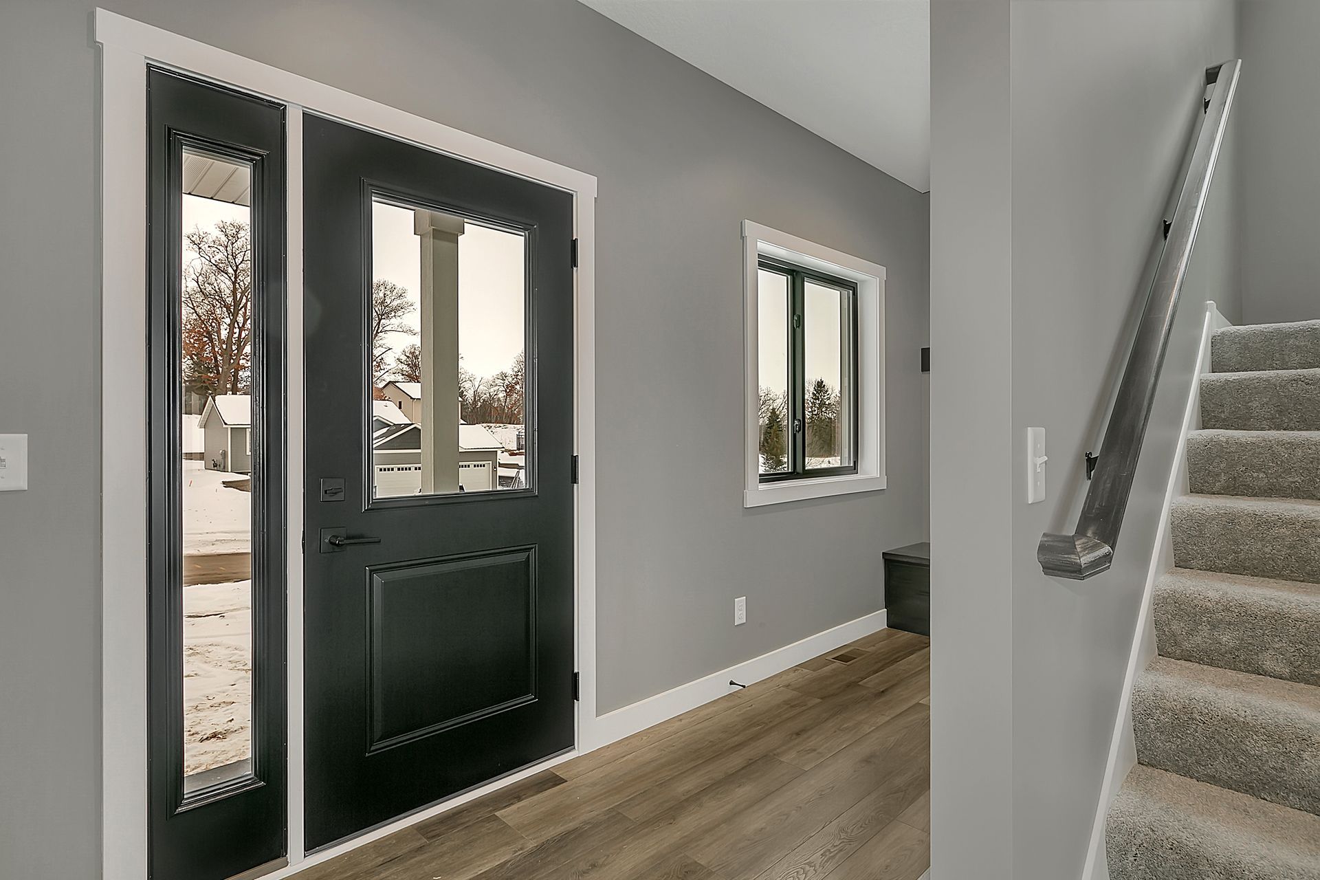 A hallway with a black door and stairs leading up to the second floor.