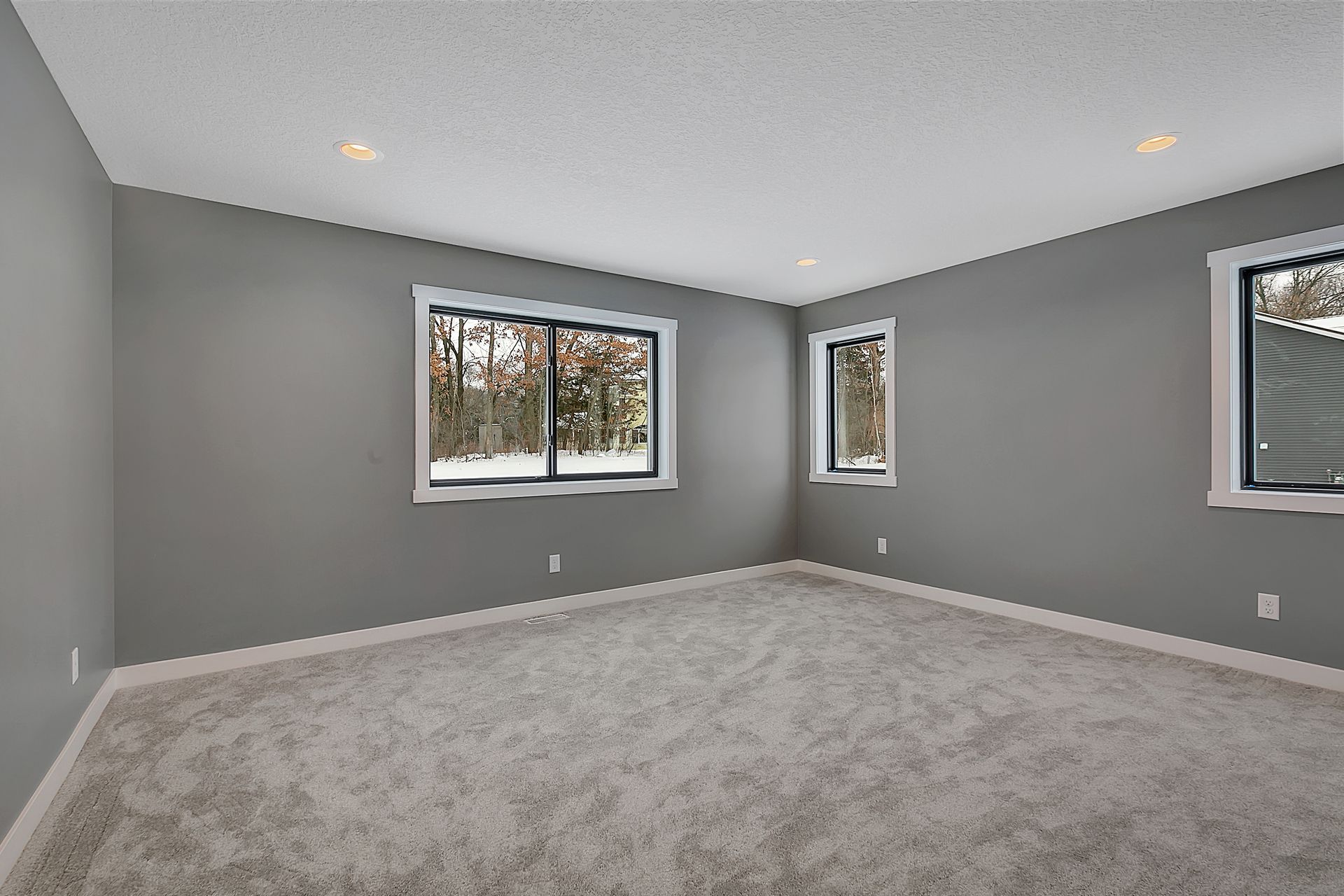 An empty room with a carpeted floor and two windows.