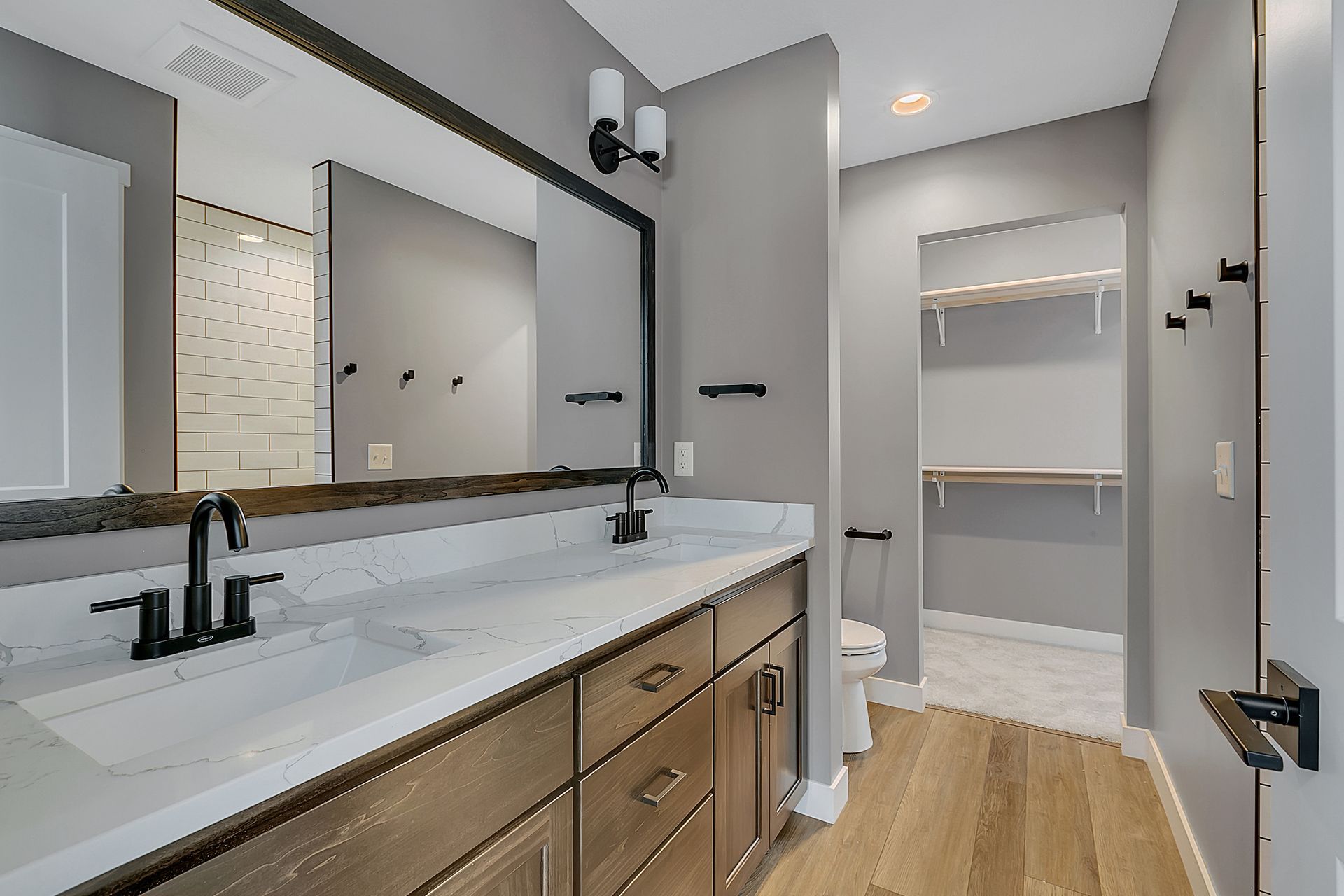A bathroom with a sink , mirror , toilet and walk in closet.