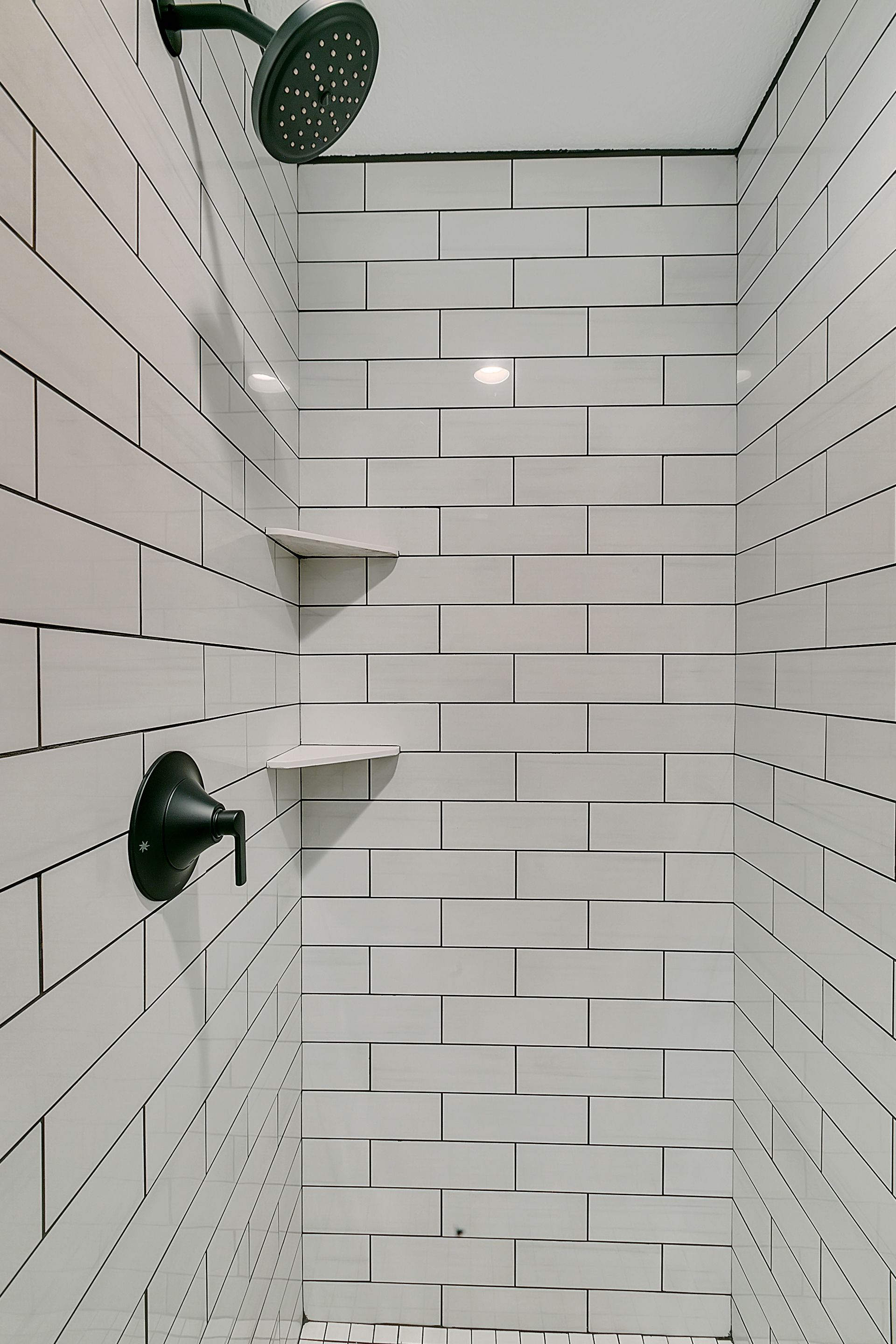 A shower with white tiles and a black shower head
