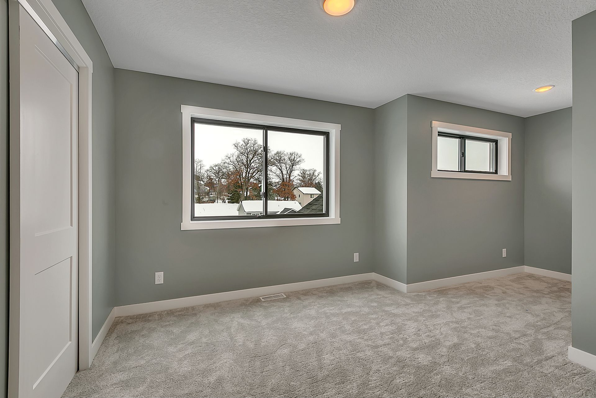 An empty room with a carpeted floor and two windows.
