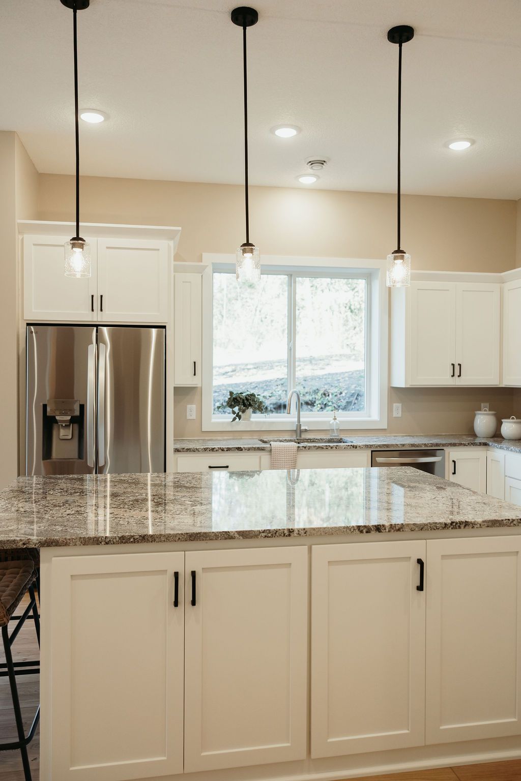 Kitchen with white cabinets, granite countertop island, stainless steel refrigerator, and three pendant lights.