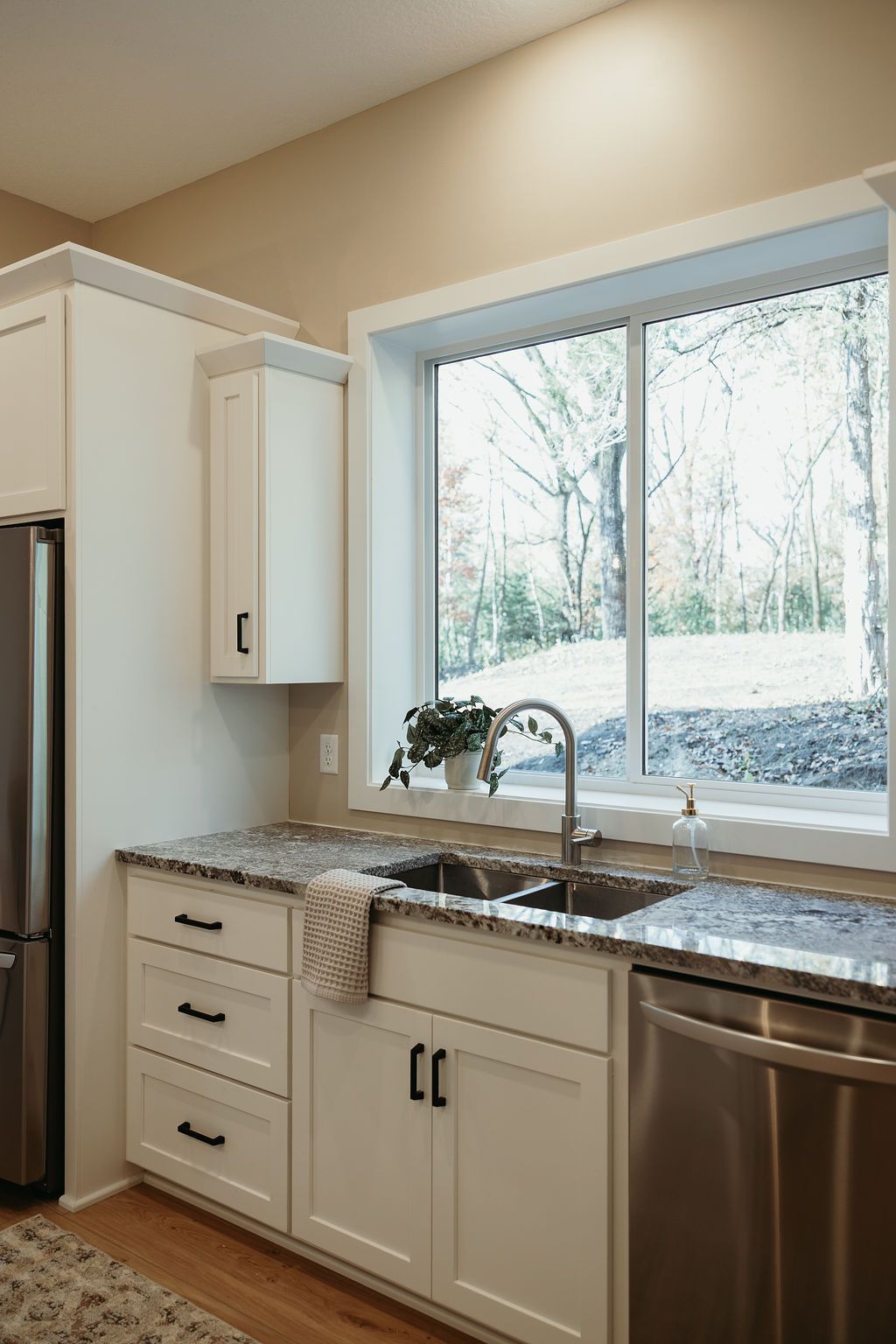 Kitchen with white cabinets, granite countertop, stainless steel appliances, and a window overlooking trees.