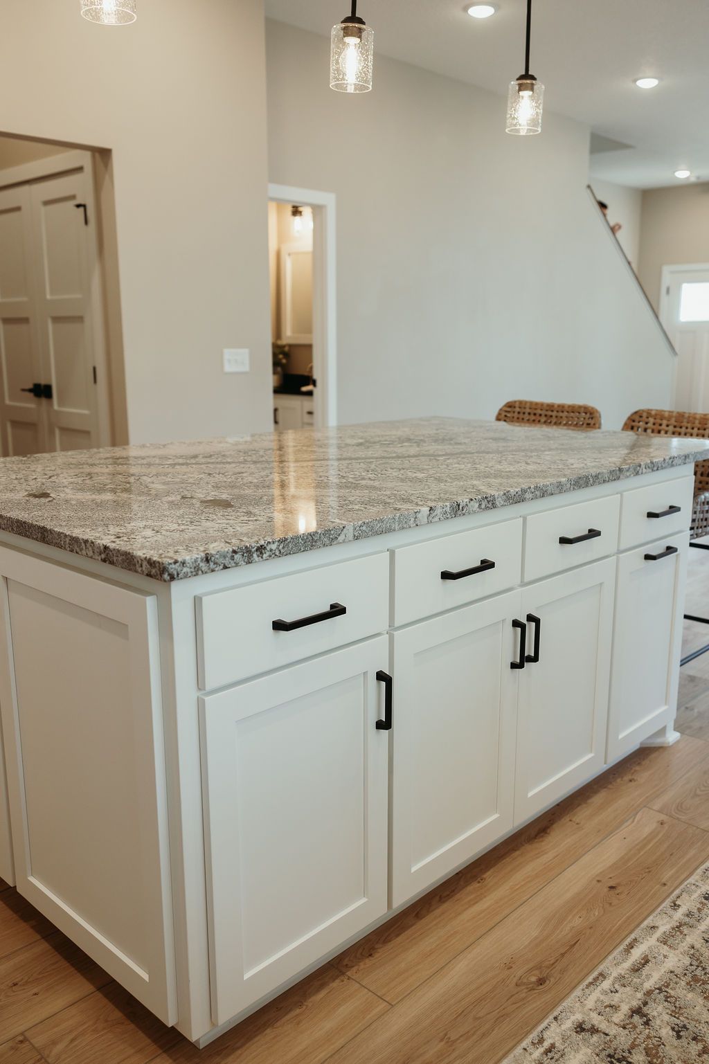 White kitchen island with granite countertop, black hardware, and wood flooring.
