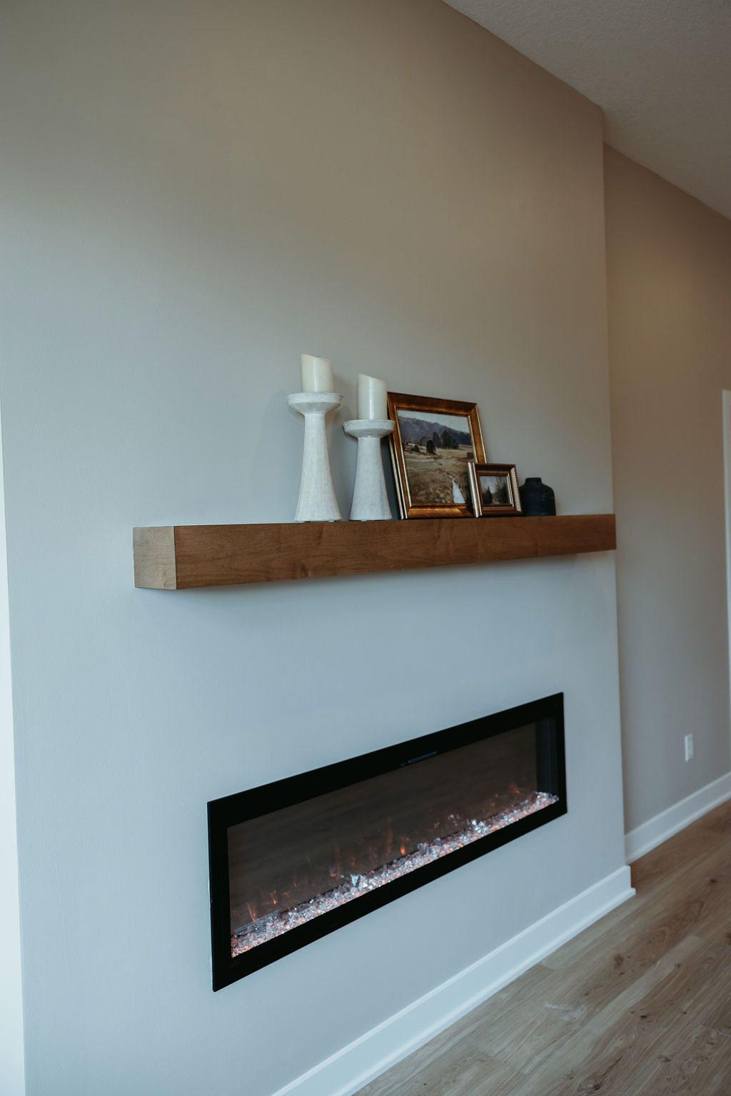 Modern fireplace with a wooden mantel holding candles and pictures, against a gray wall.