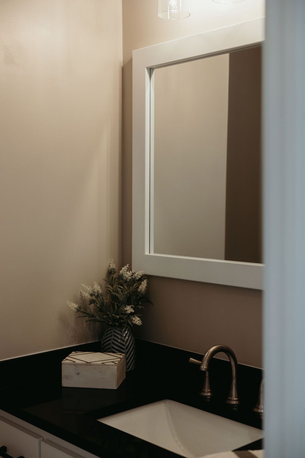 Bathroom with white-framed mirror, black countertop, white sink, and neutral walls.