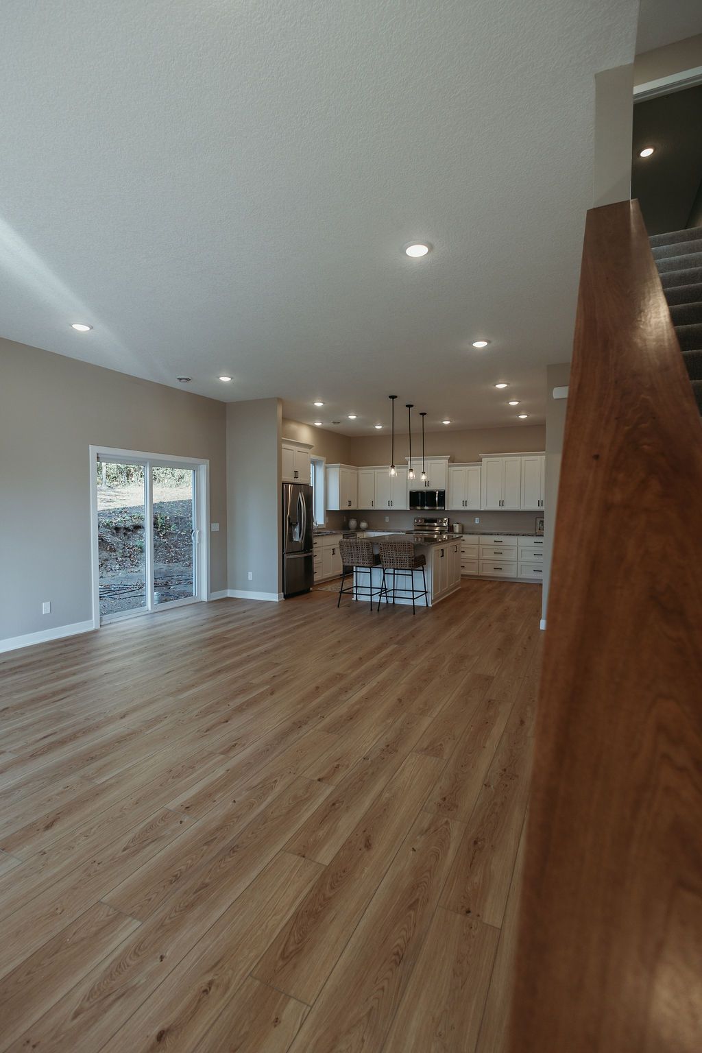 Spacious open-concept kitchen and living area with wood-look flooring, white cabinets, and stainless steel refrigerator.