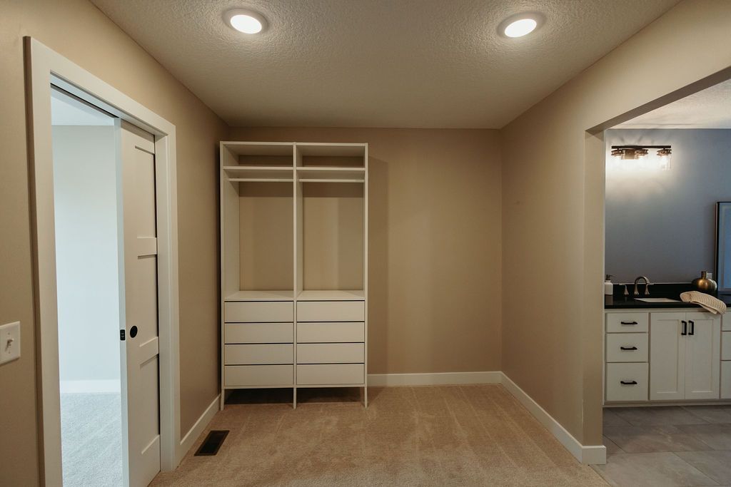 Empty beige bedroom with closet and doorway to a bathroom with a vanity.