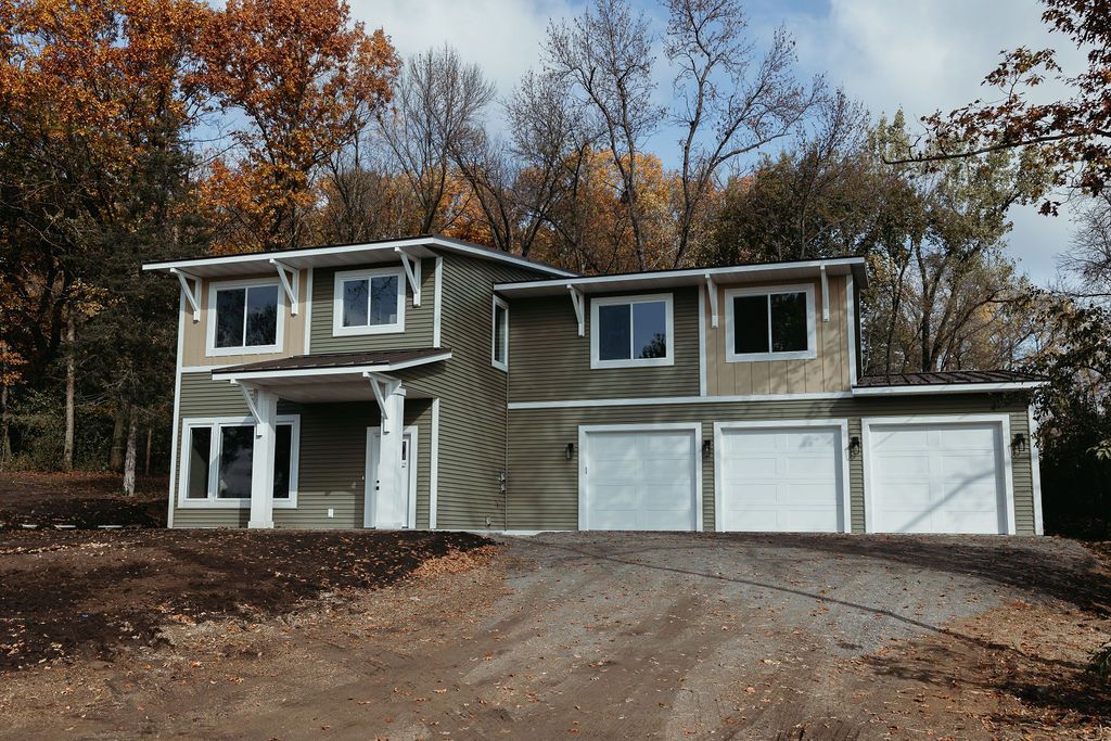 Two-story house with green siding, white trim, and a three-car garage, driveway leading up.