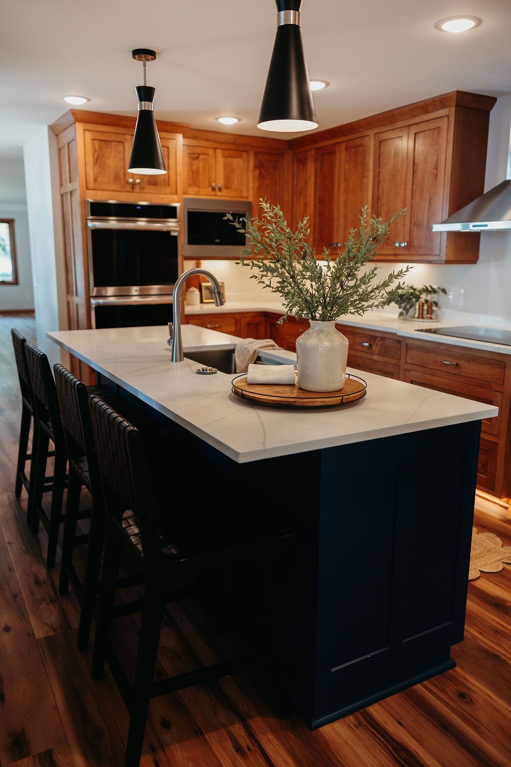 Kitchen with wood cabinets, navy island, marble countertop, and black pendant lights.