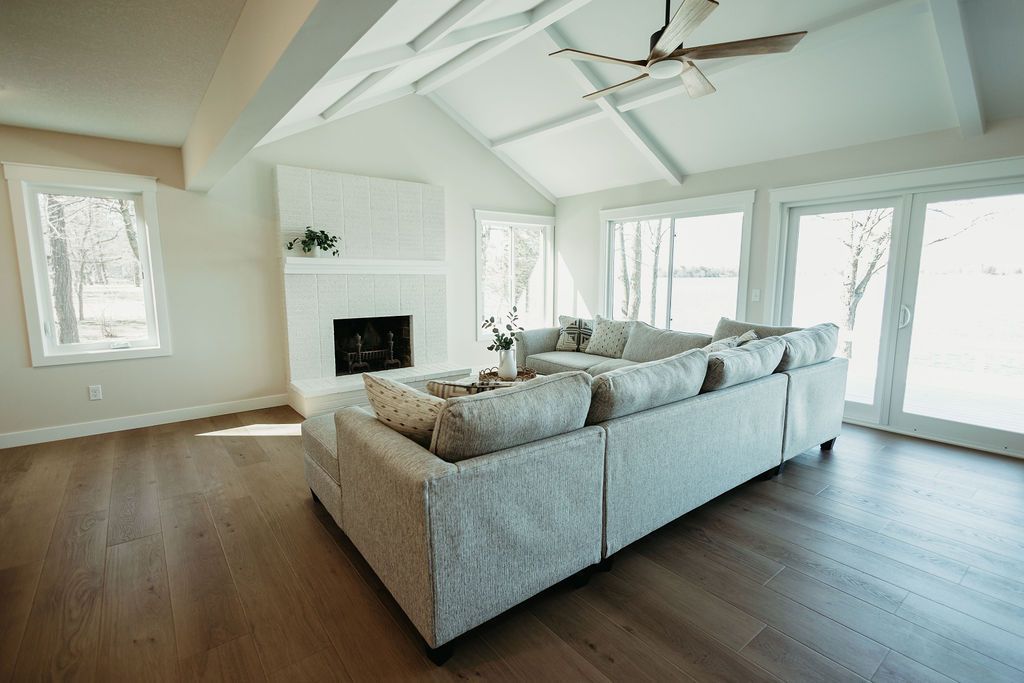 Bright modern living room with gray sectional sofa, fireplace, wood floors, and large windows