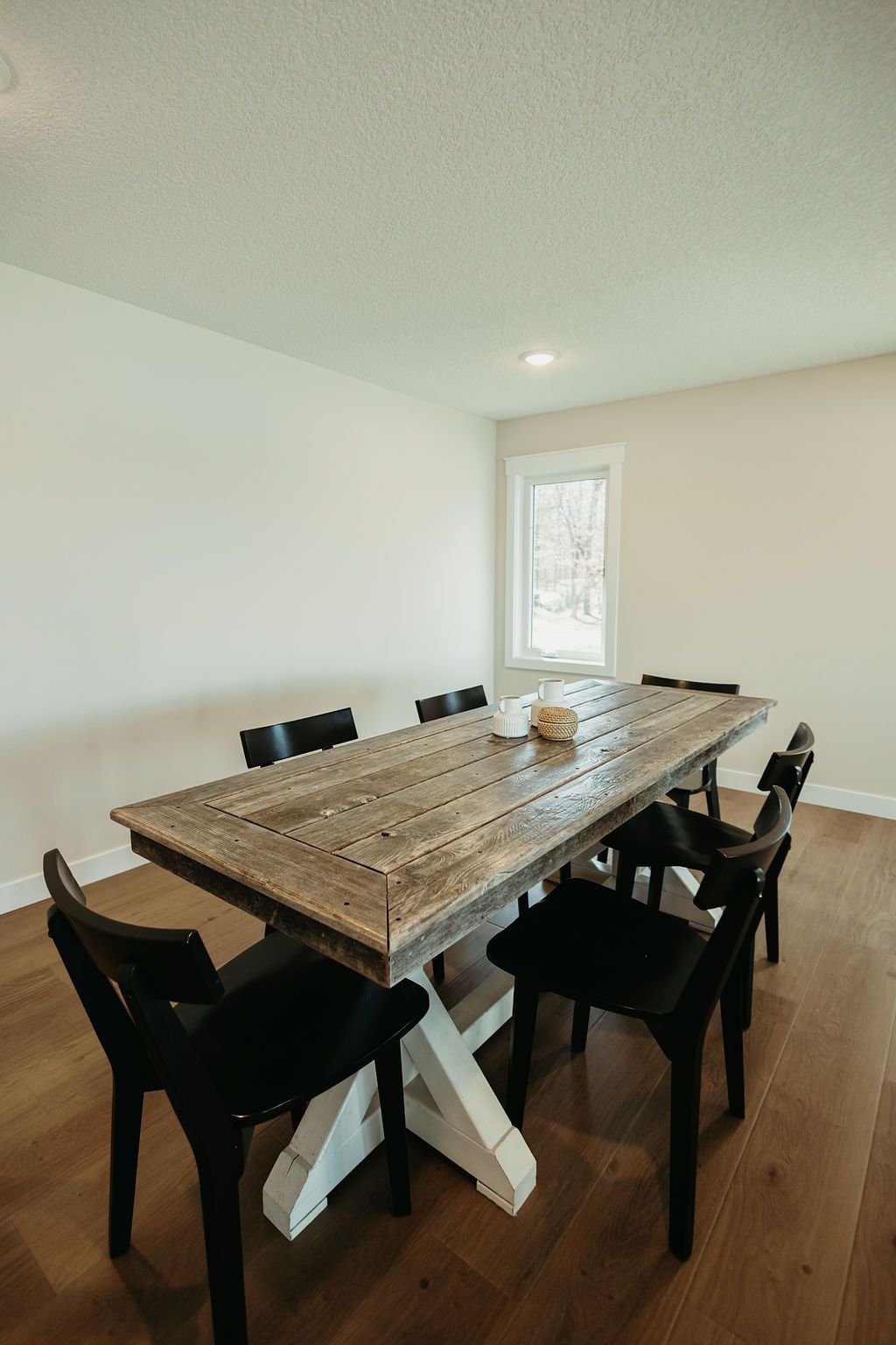 Modern dining room with a large wooden table, black chairs, and white walls by a small window