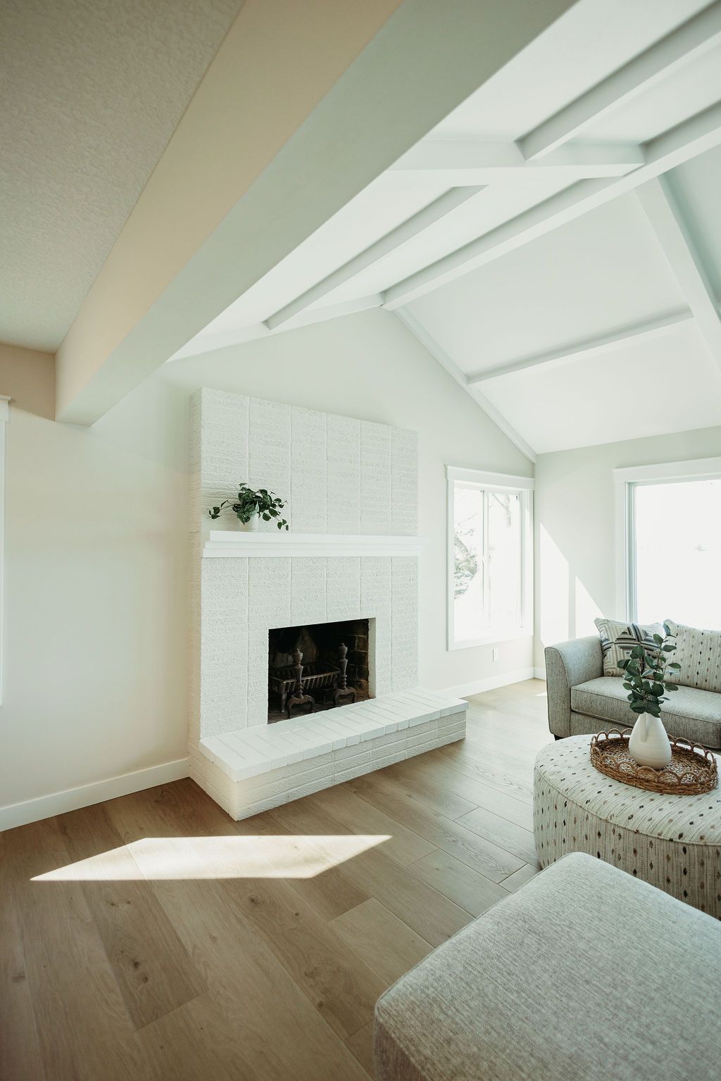 Bright, modern living room with white fireplace, high vaulted ceiling, and sunlight on wood floors