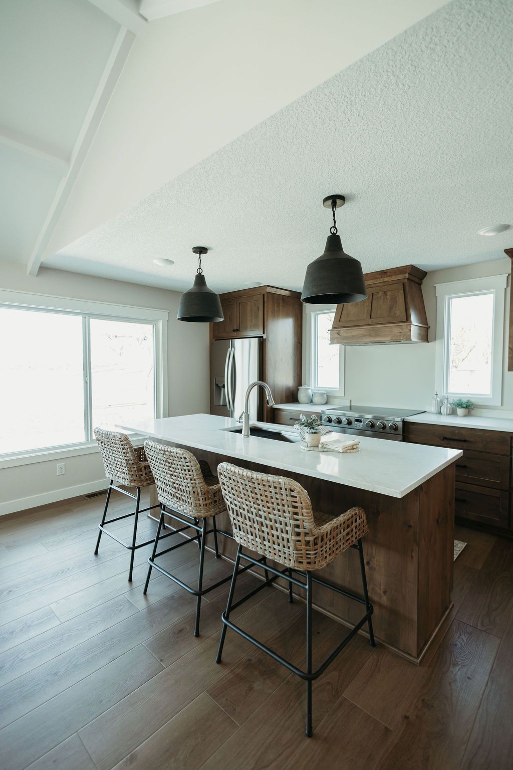 Bright kitchen island with woven stools, black pendant lights, and large windows in a modern home
